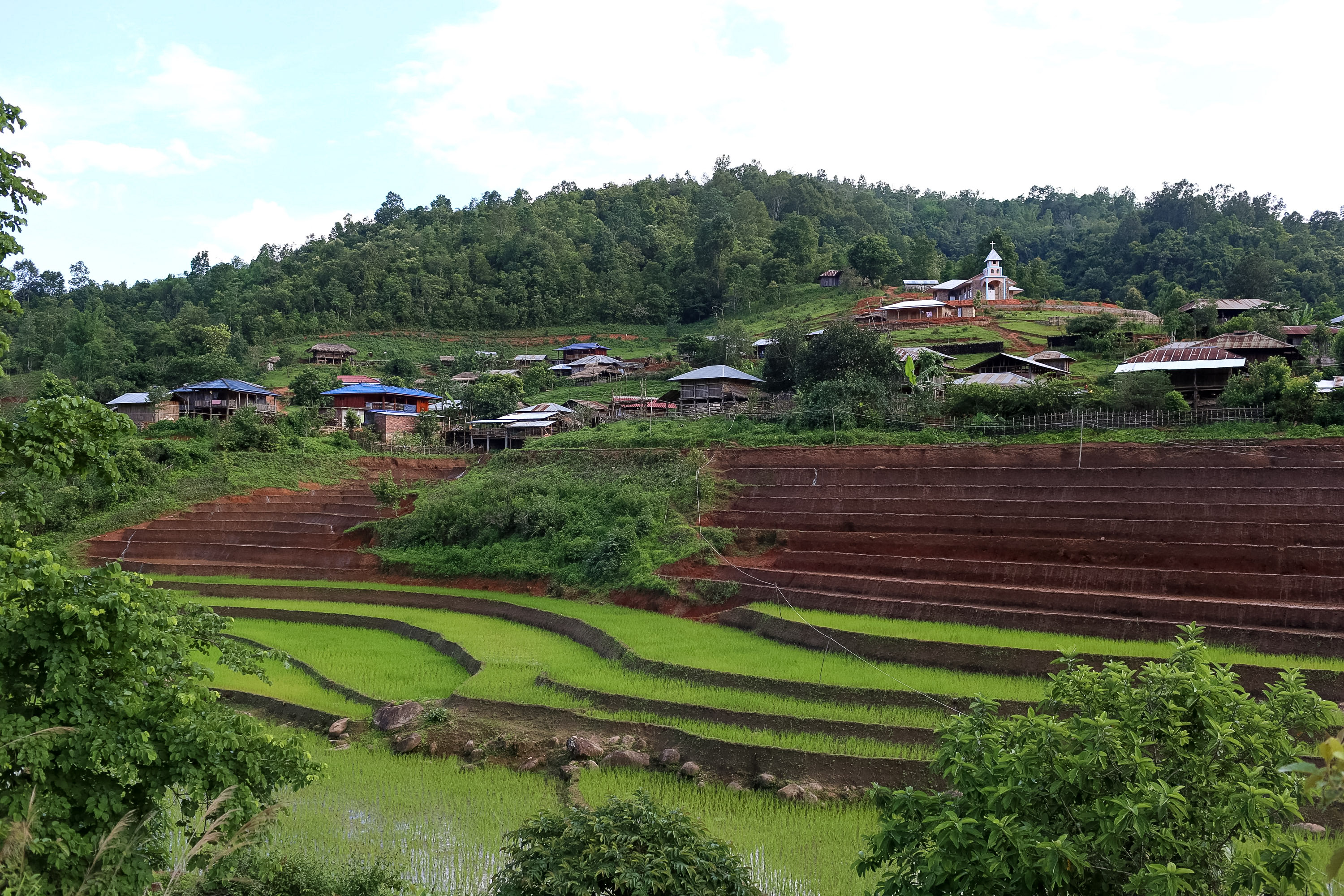 Terraced rice fields step down a hillside village dotted with houses and a small church