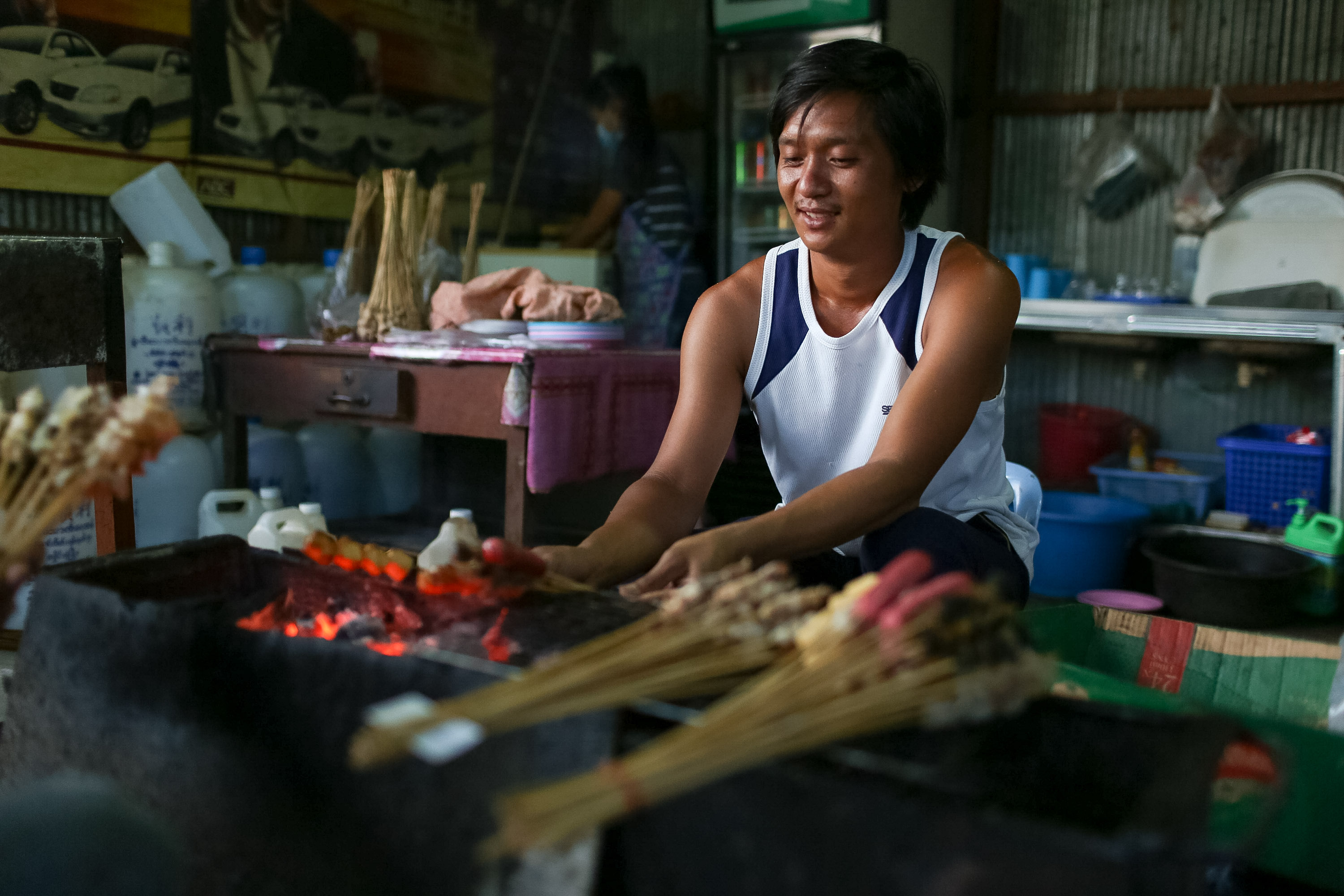A vendor grills skewers over hot coals at a street food stall