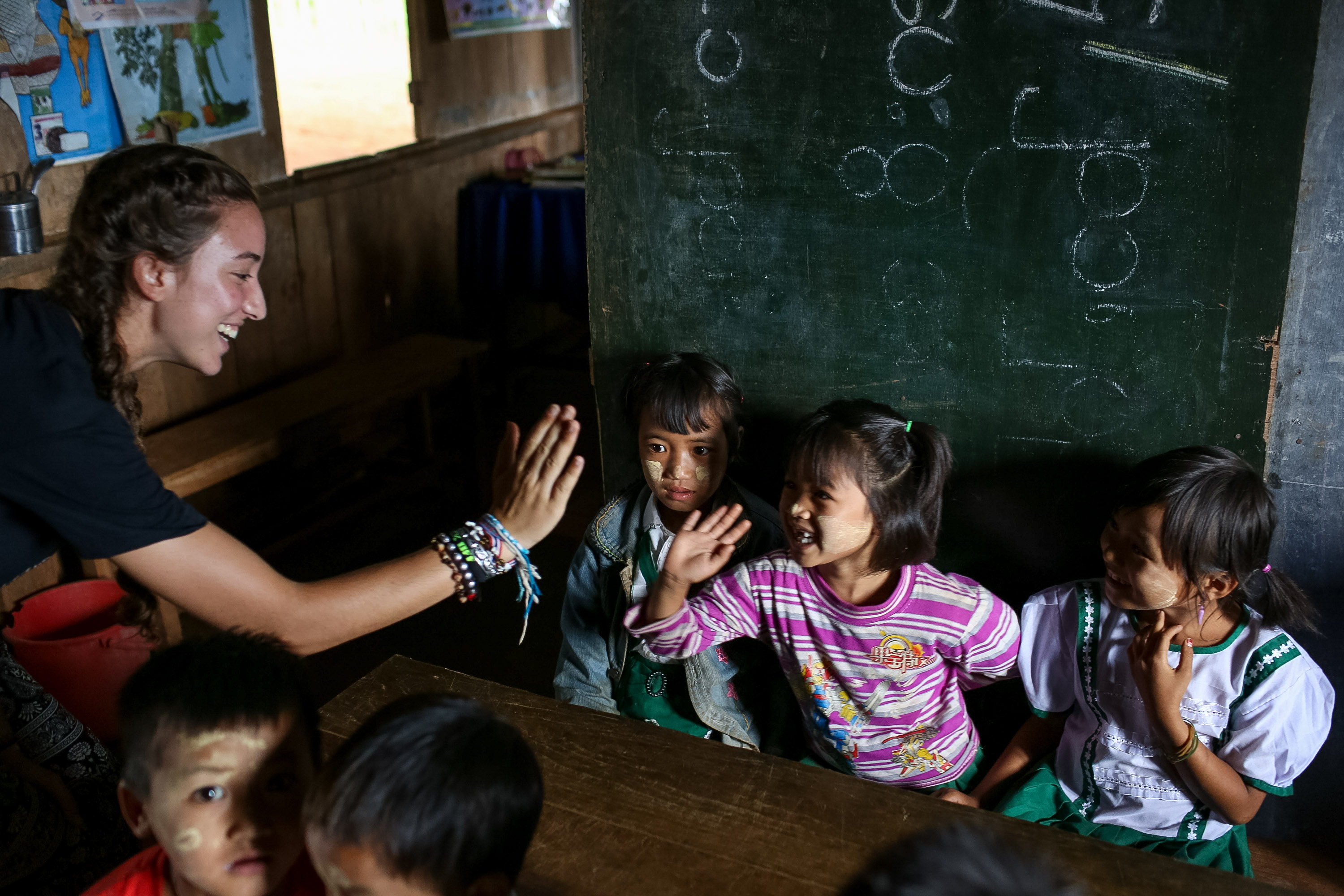A student high-fives local children in a classroom in Myanmar, in front of a chalkboard