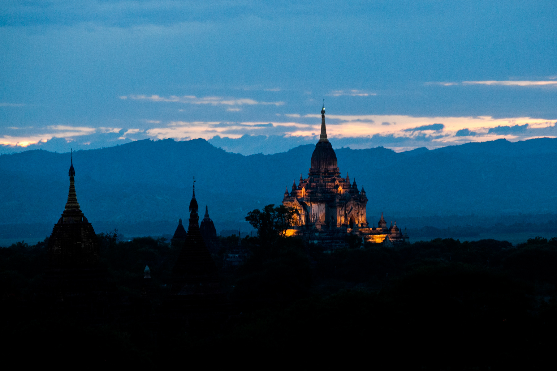 Illuminated temple spires rise against silhouetted hills at dusk in Bagan