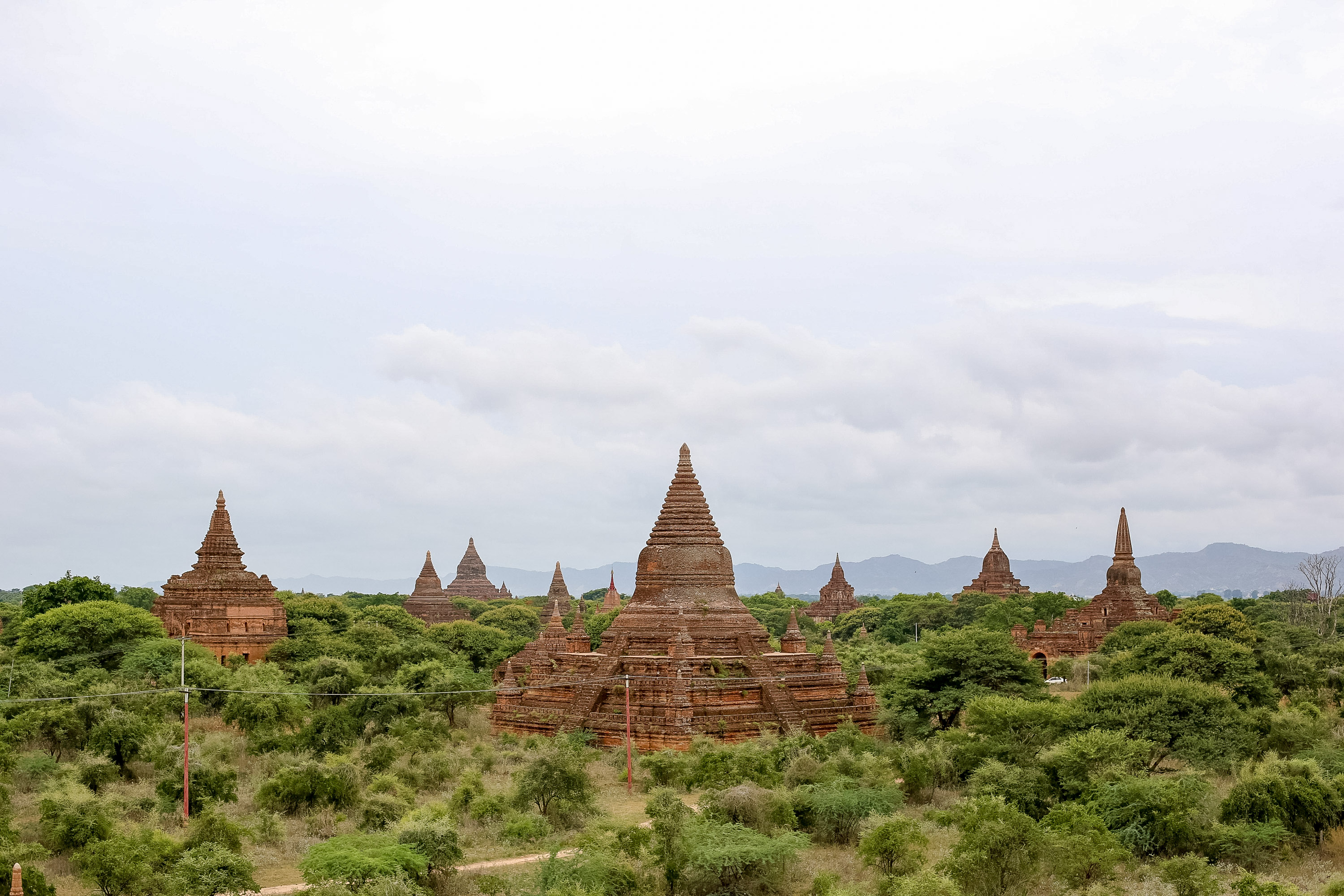 Ancient brick temples rise above green forest under a cloudy sky