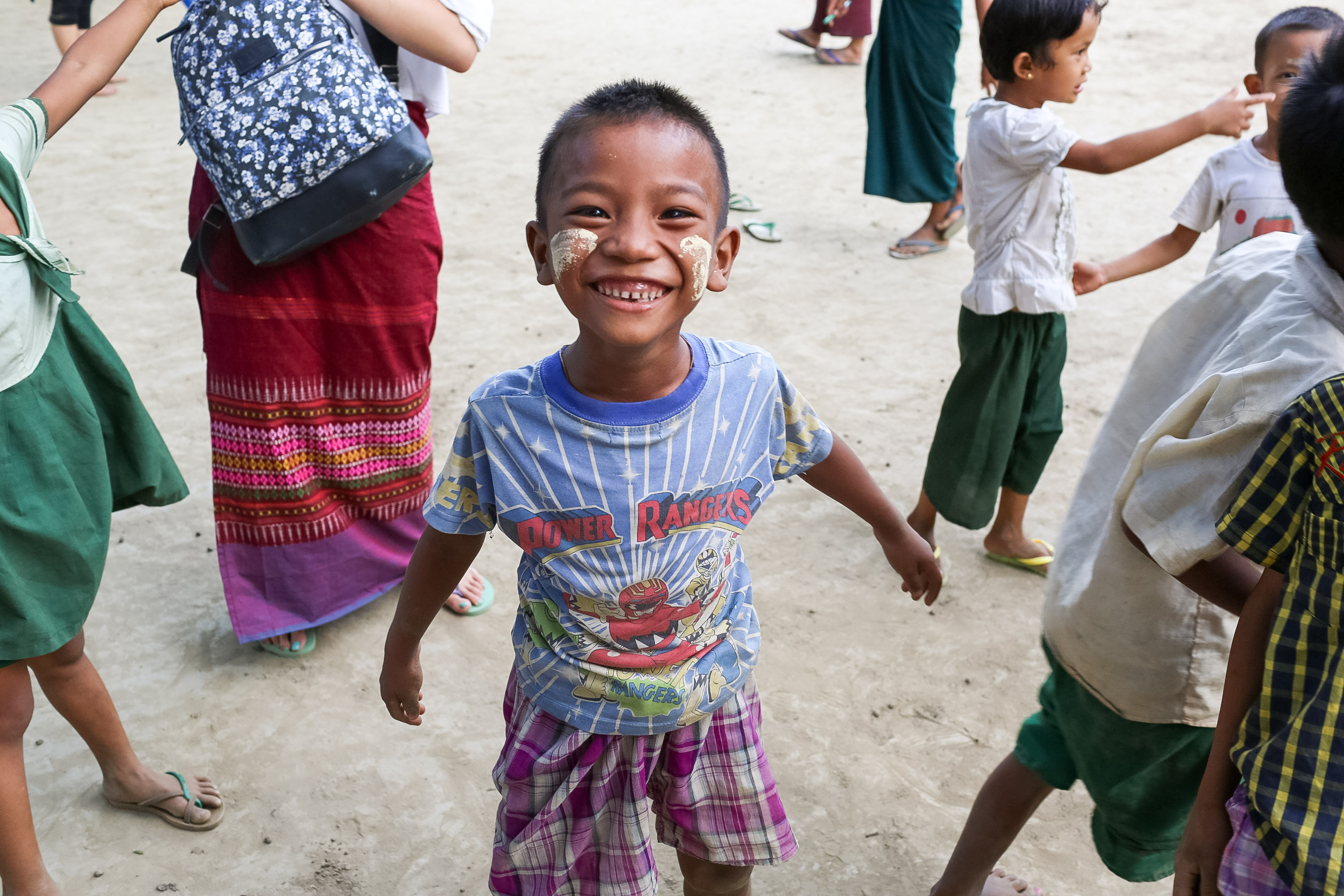 On this school trip, a boy with painted cheeks smiles while playing outdoors with other children