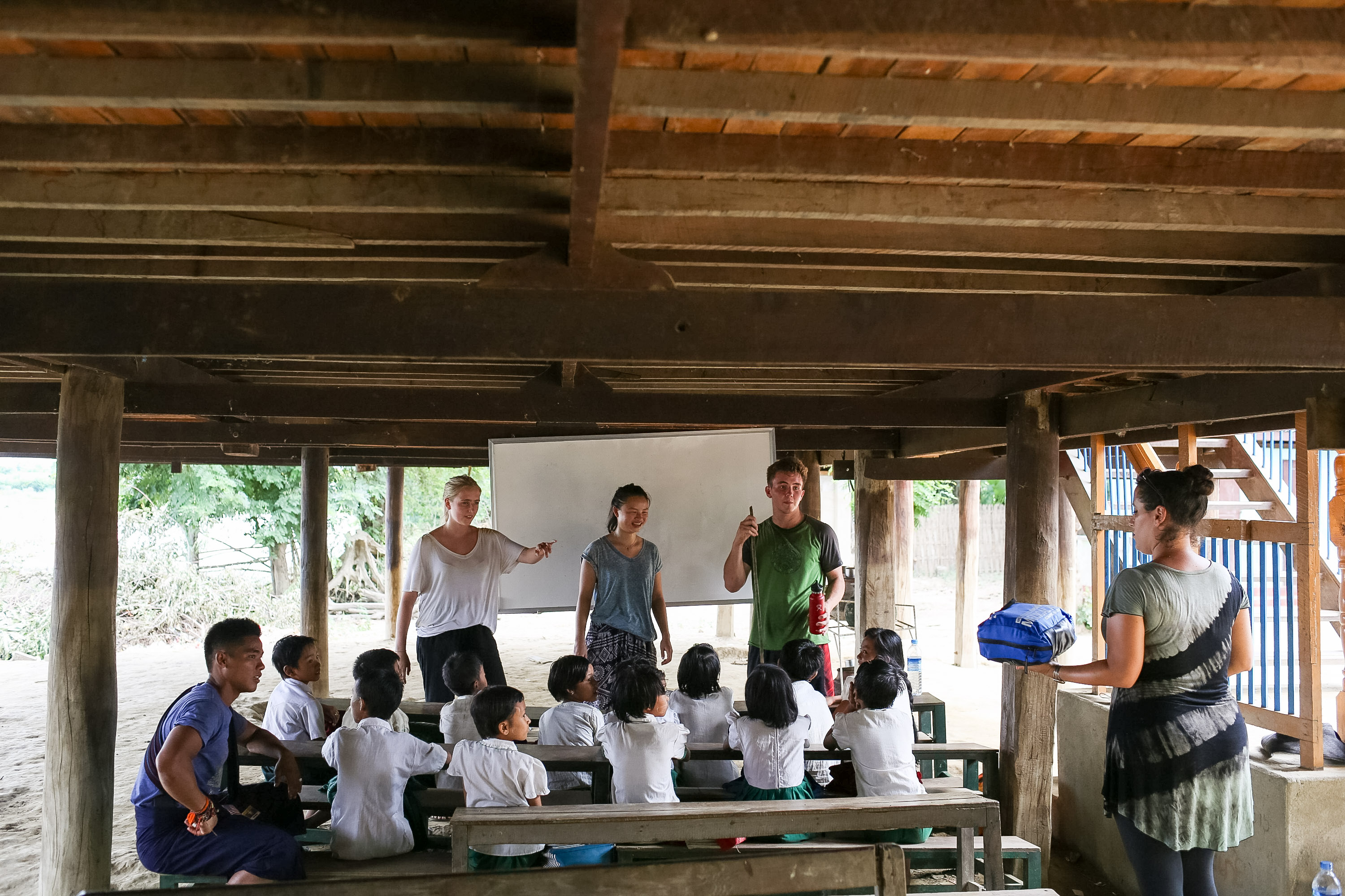 Students lead a lesson for young children seated at benches in an open-air wooden pavilion