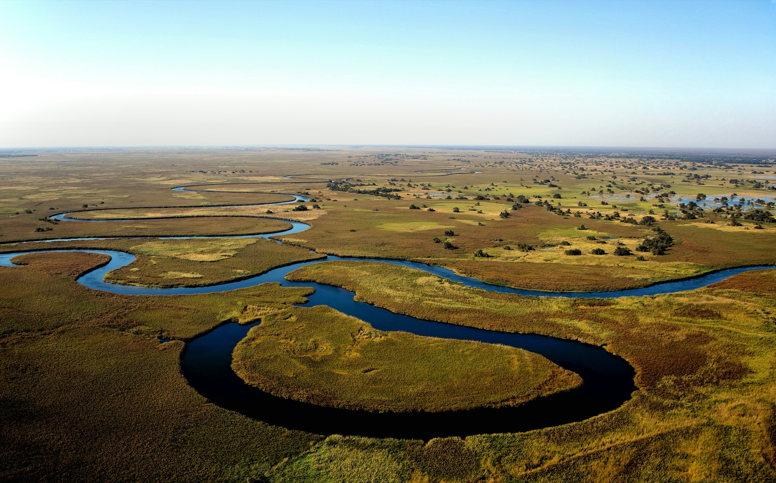 An aerial view of a river winding in tight loops through green and gold floodplain, with islands of trees to the horizon.