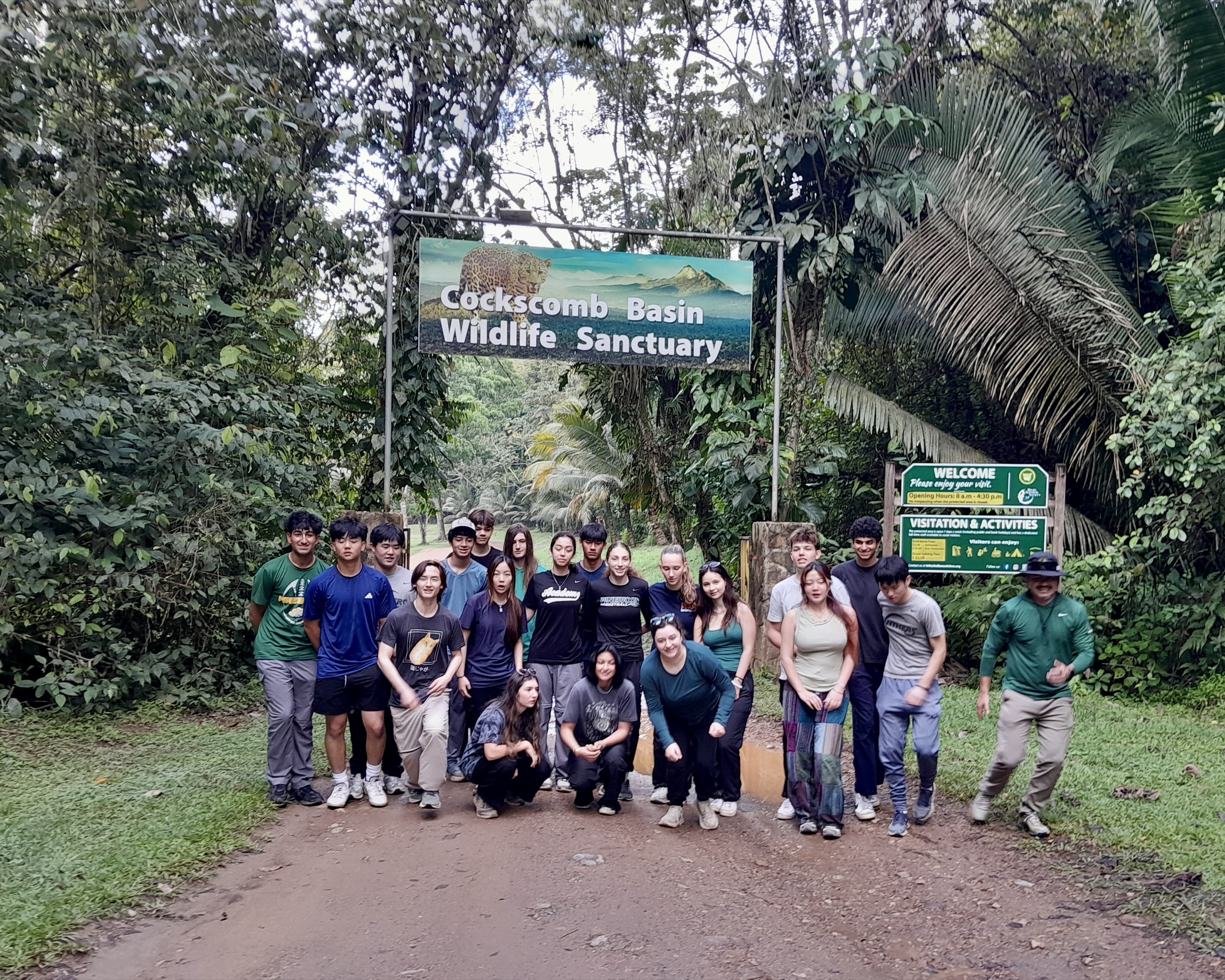 Students gather under the Cockscomb Basin Wildlife Sanctuary entrance sign on a jungle road in Belize