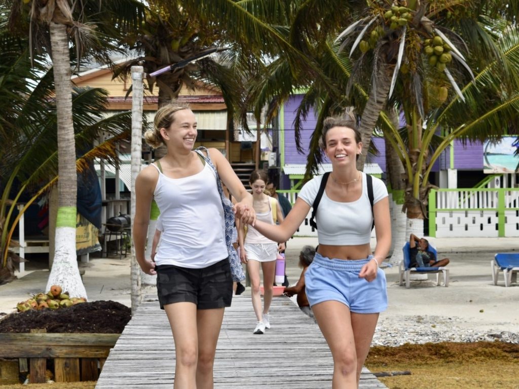 Two smiling students walk hand in hand on a boardwalk by the beach in Belize during a spring break teen tour.