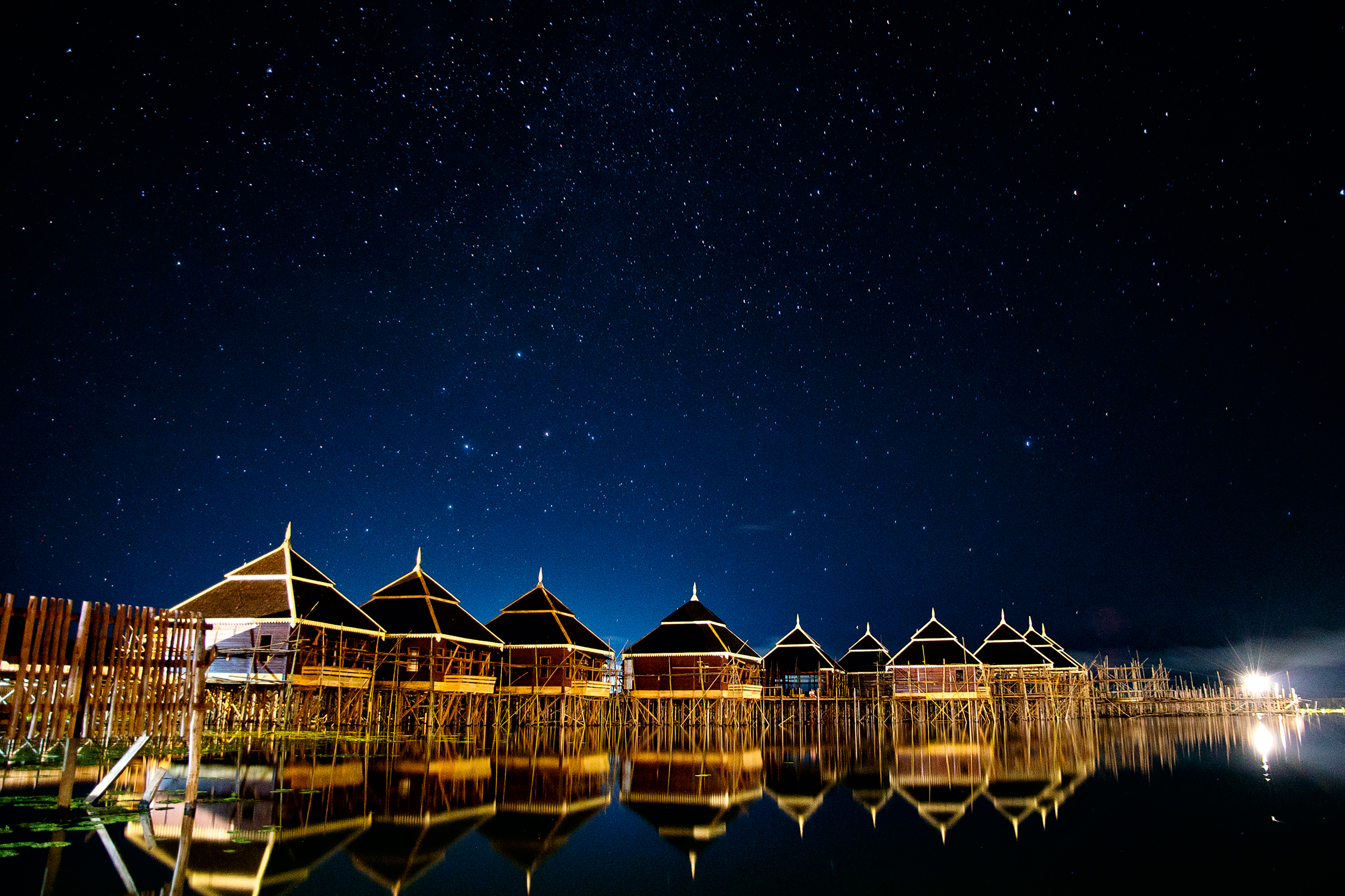 Stilted bamboo huts glow at night over Inle Lake beneath a star-filled sky