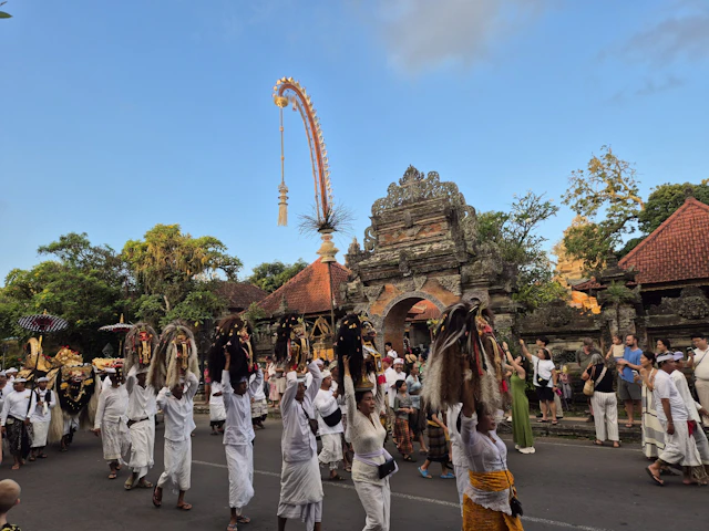 A procession of people in white ceremonial dress passes a carved stone temple gate in Ubud, Bali