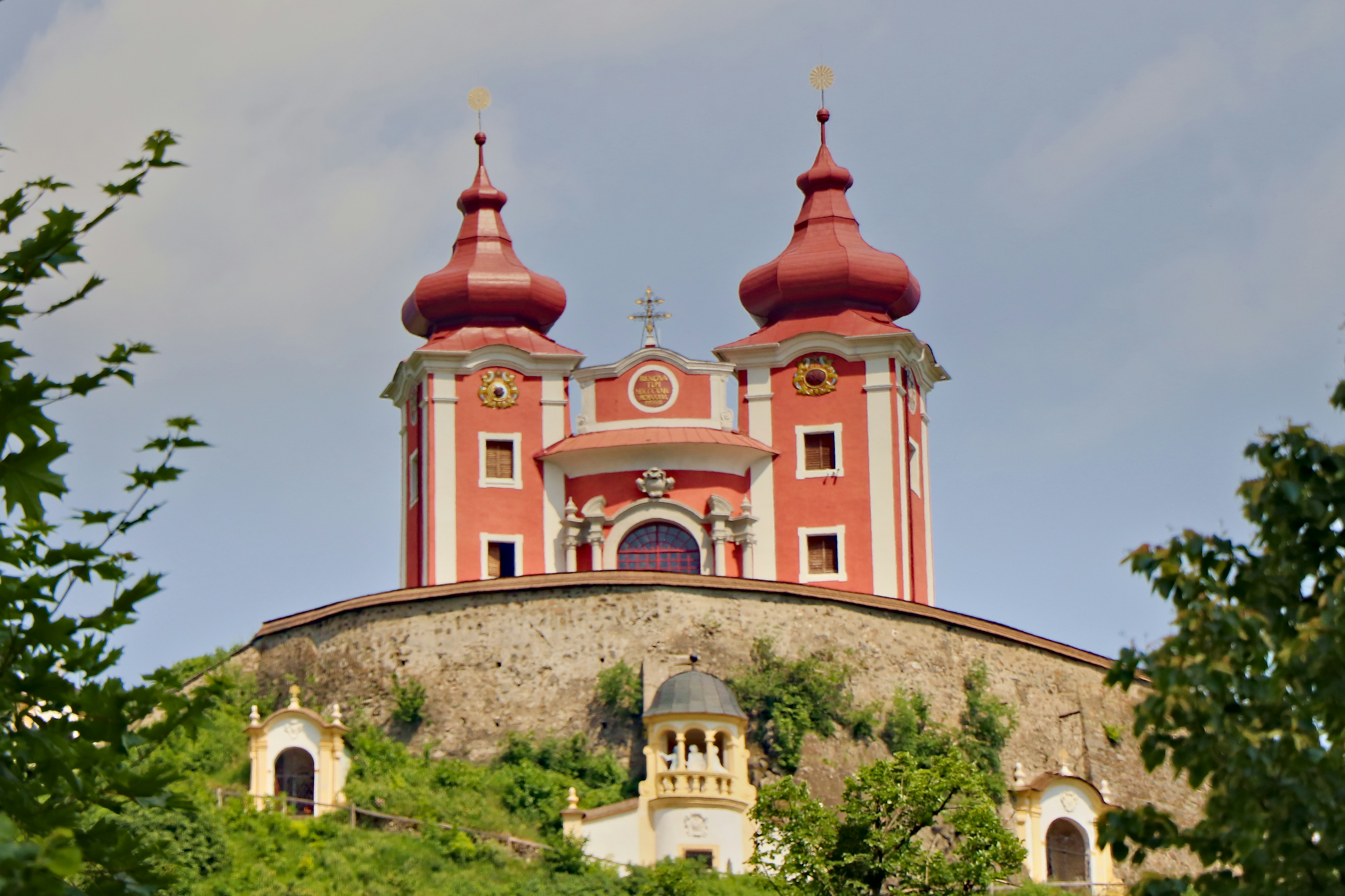 The twin red domes of the Calvary church in Banská Štiavnica on its hilltop above a stone retaining wall.