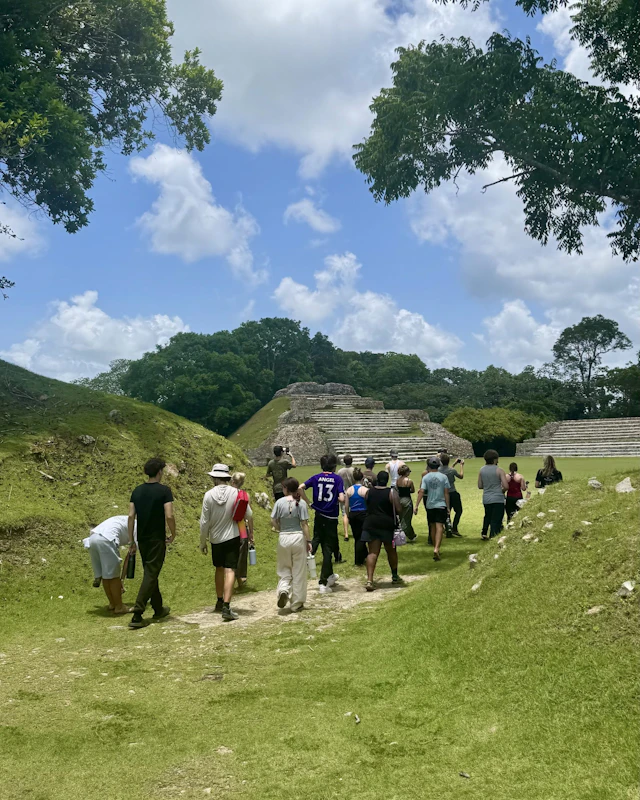 A line of teen travelers walks across a Maya site in Belize toward a stepped stone pyramid
