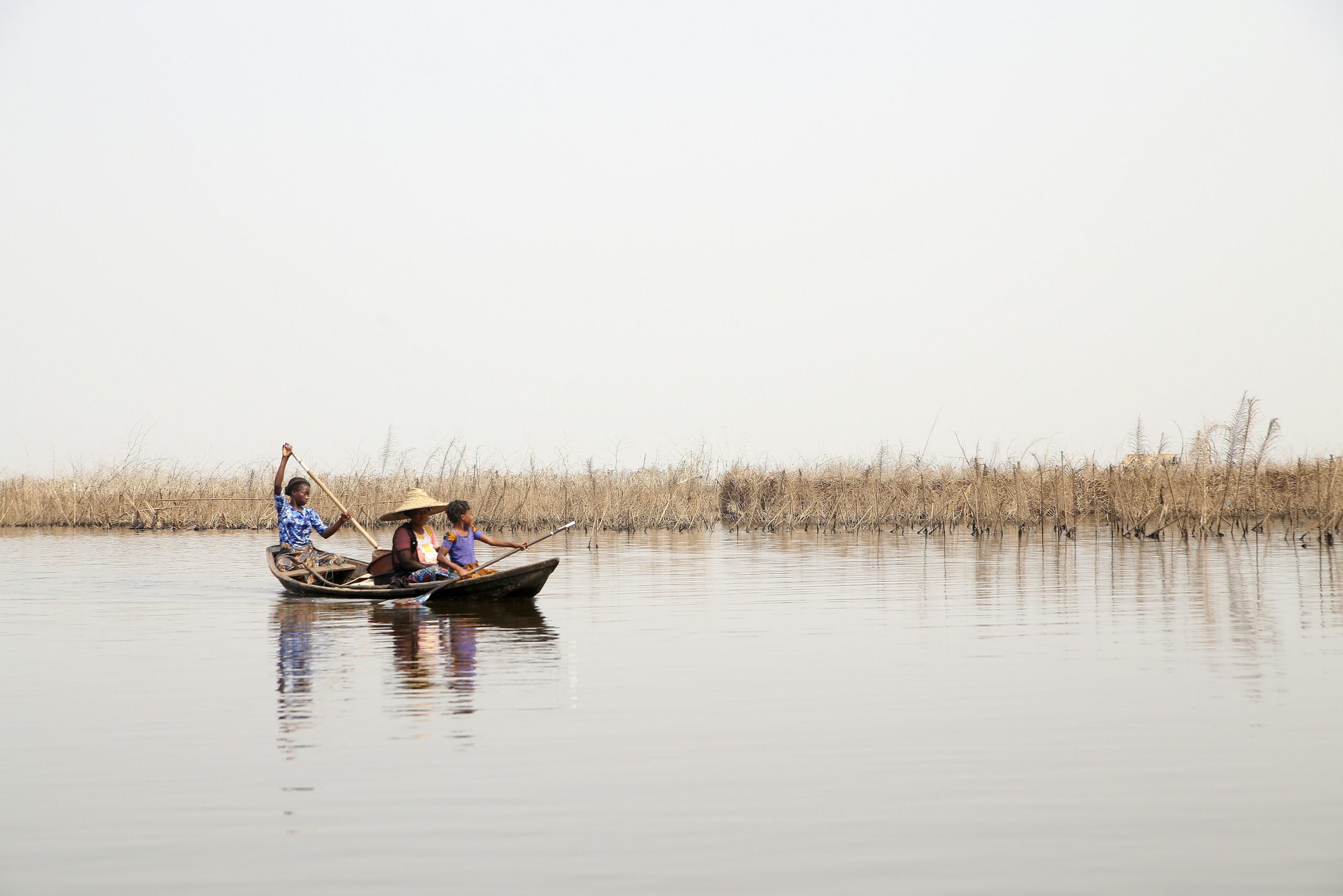 A family paddling a canoe through calm waters surrounded by dried vegetation, reflecting rural life in Benin's wetlands.