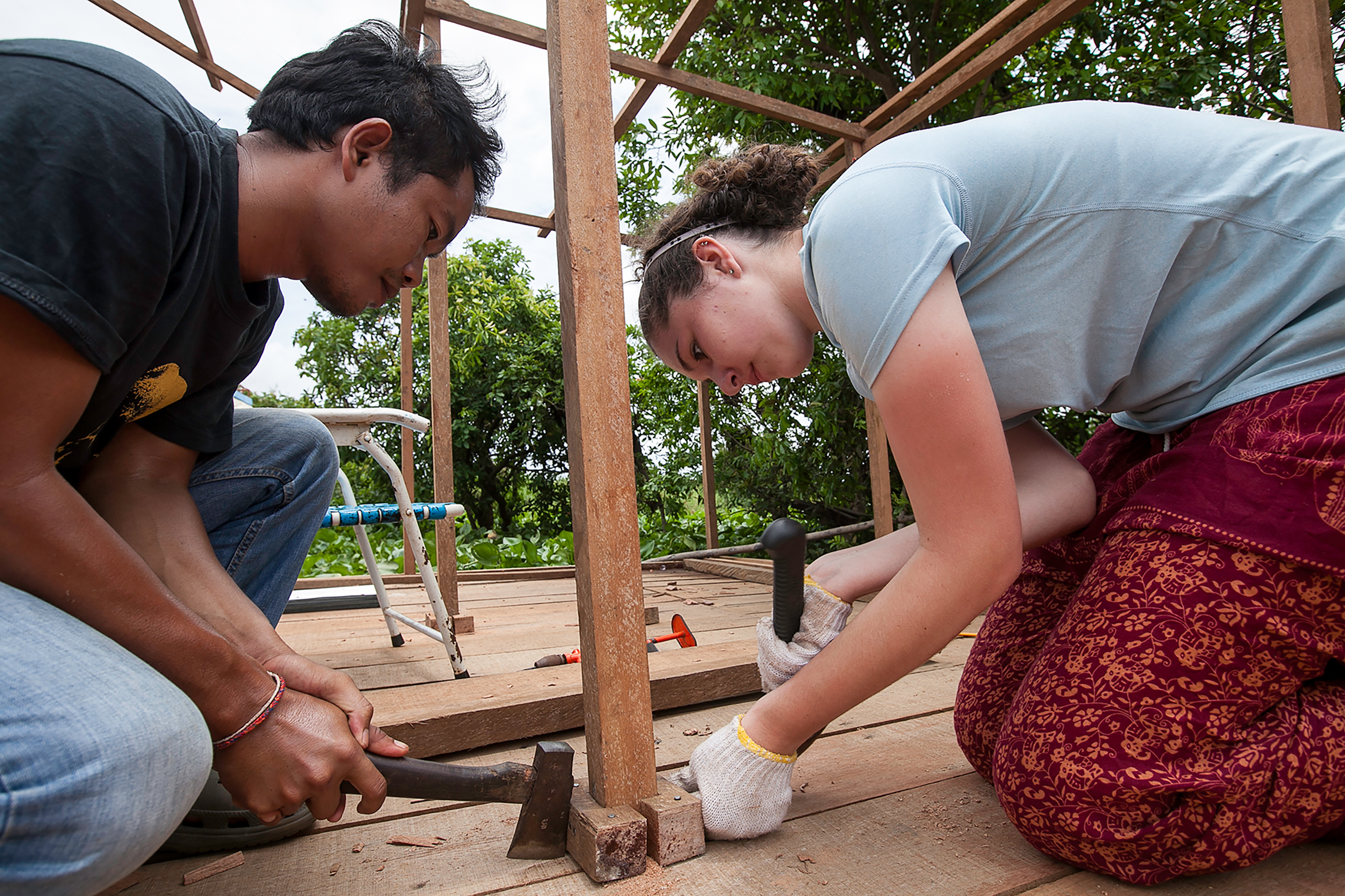 Students work together nailing wooden boards on a raised platform construction site