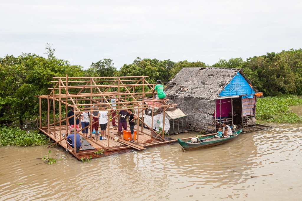 Students in Cambodia help frame a wooden structure beside a floating house on the river