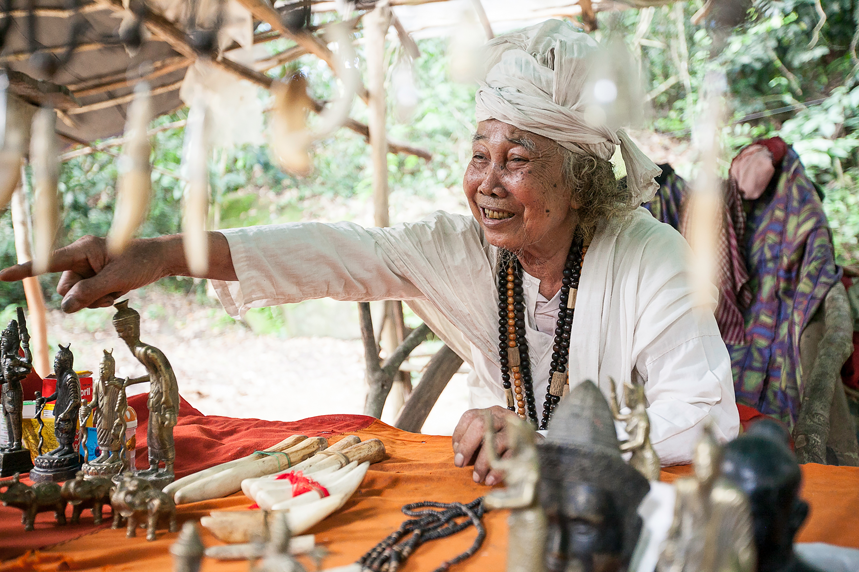 A woman in a white headwrap gestures over a table of small statues and artifacts