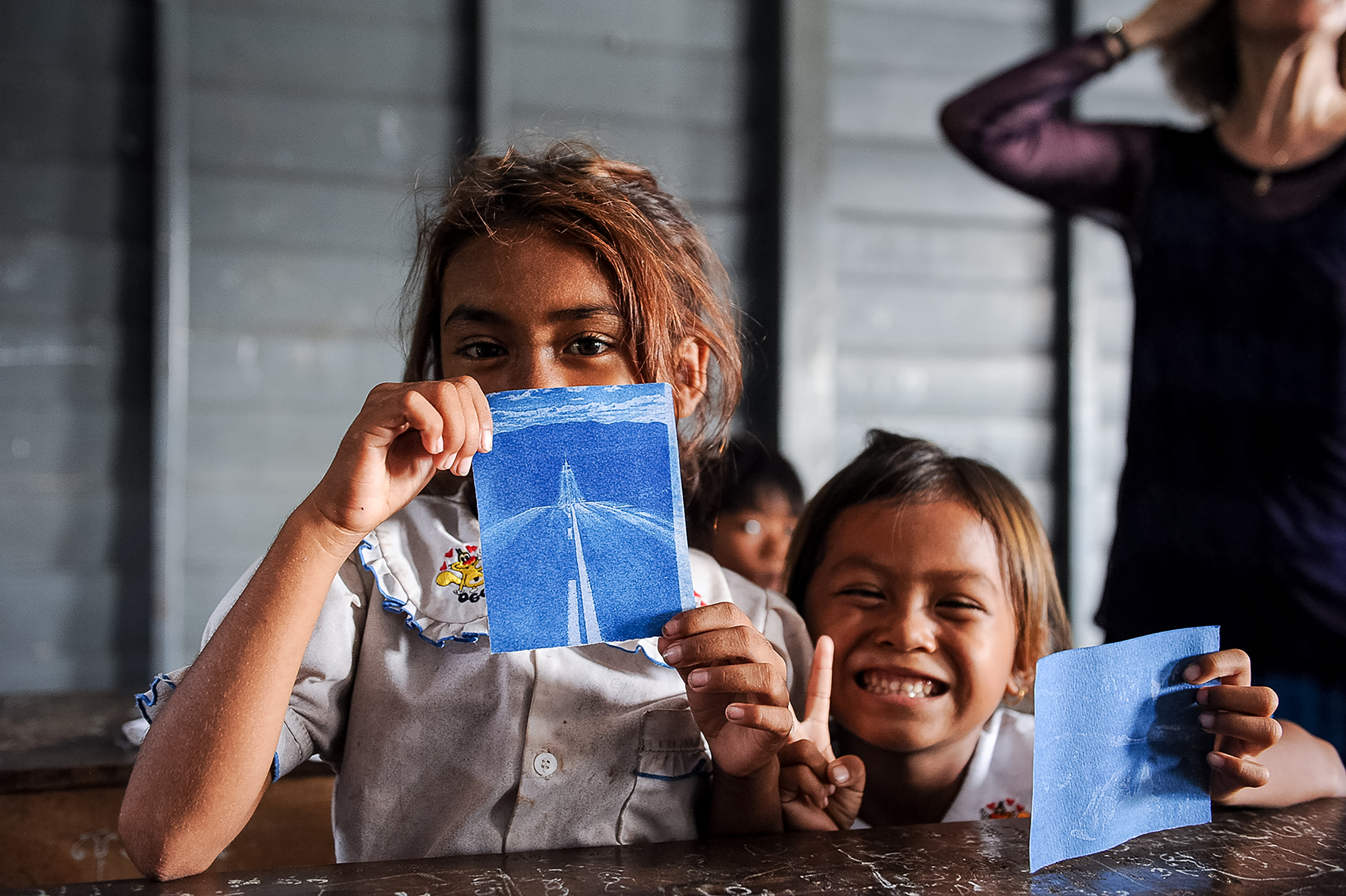 Local children in school uniforms show off cyanotype prints they made in a classroom