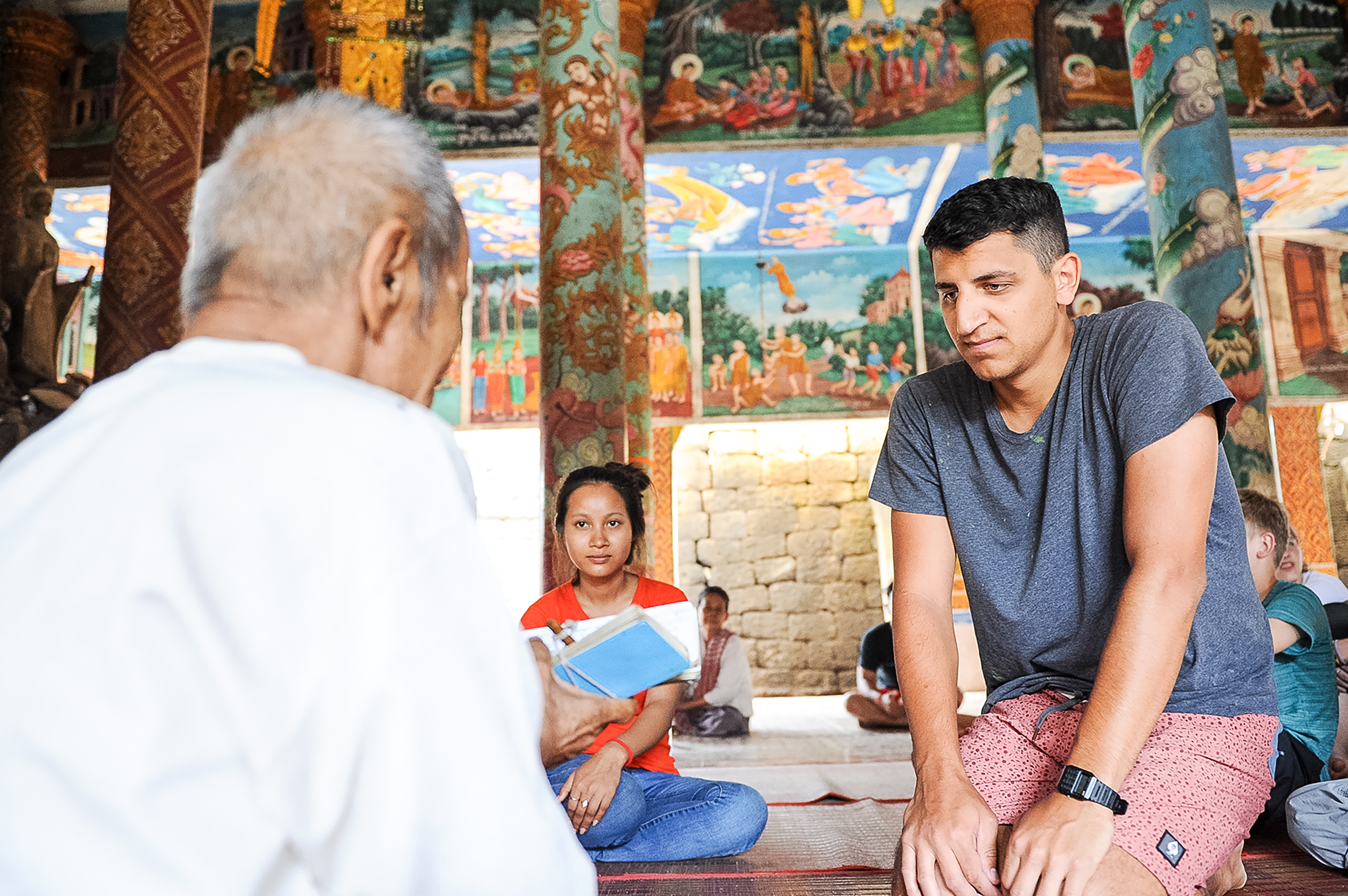 A student listens to a village elder inside a temple decorated with colorful painted murals