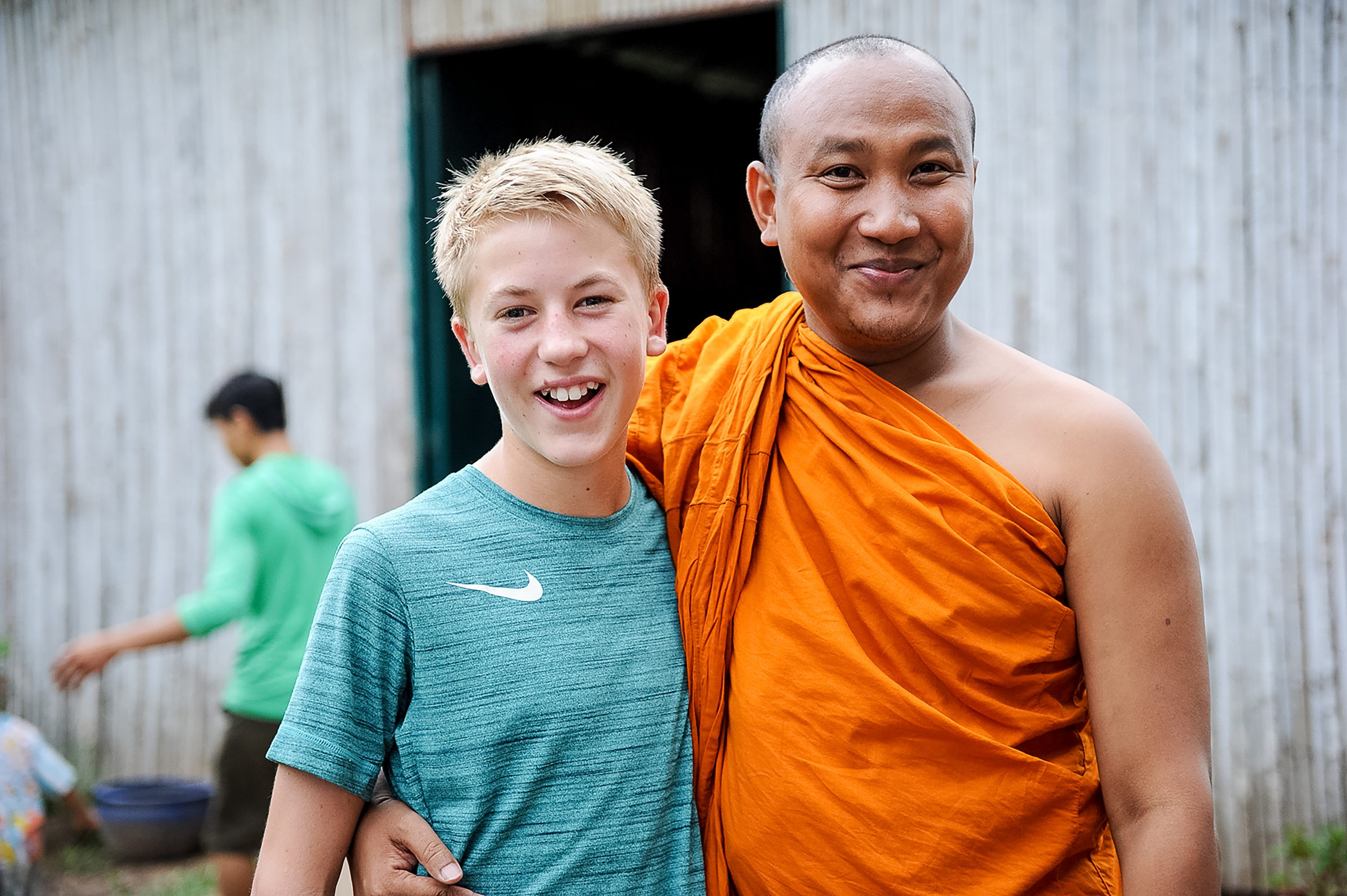 Student travelers pose with a Buddhist monk in an orange robe outside a wooden building