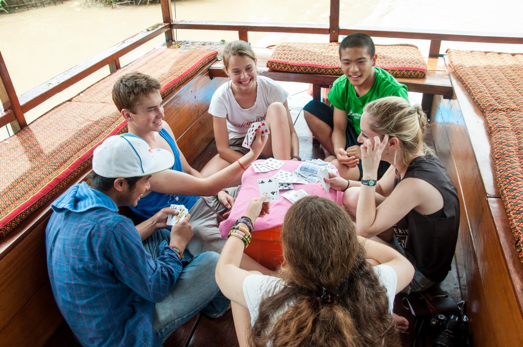 Students play cards together on a wooden boat