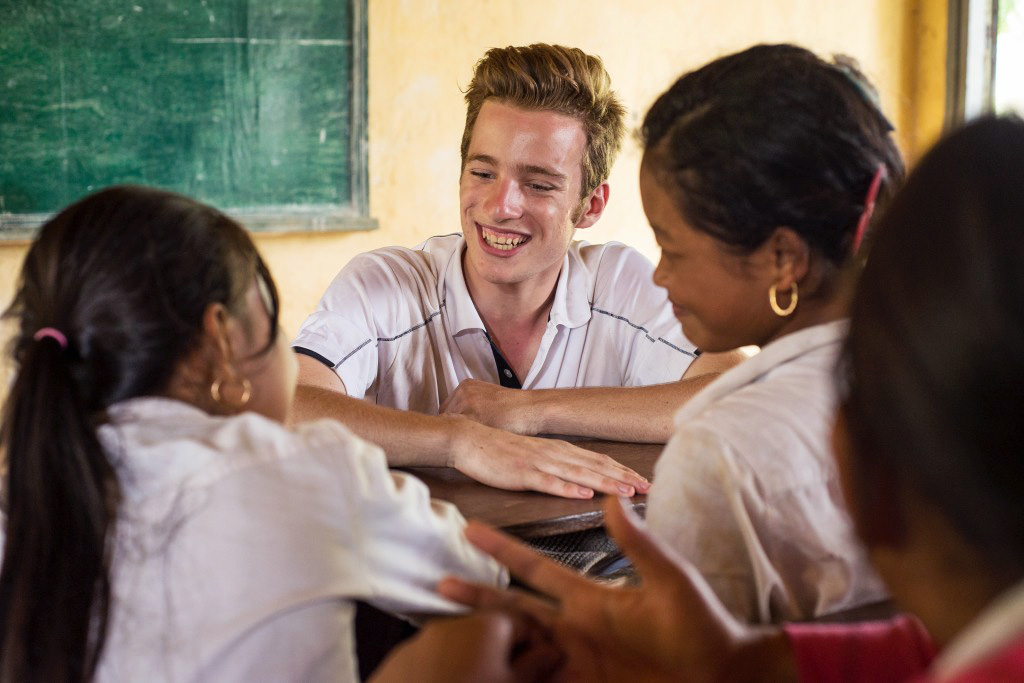 A student laughs with local students gathered around a classroom desk