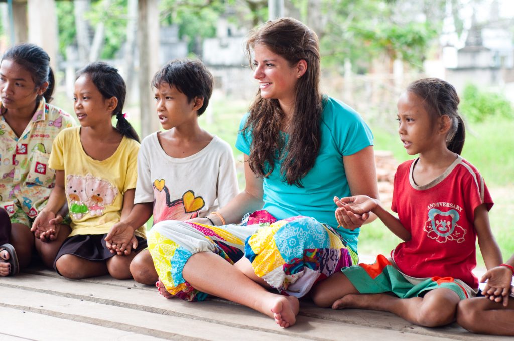 A student sits and talks with local children on a wooden porch in Cambodia