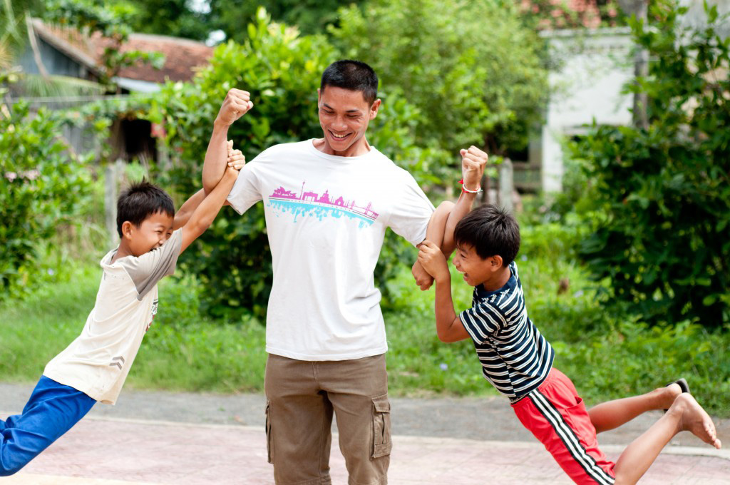 A man lifts children by their arms as they play outdoors