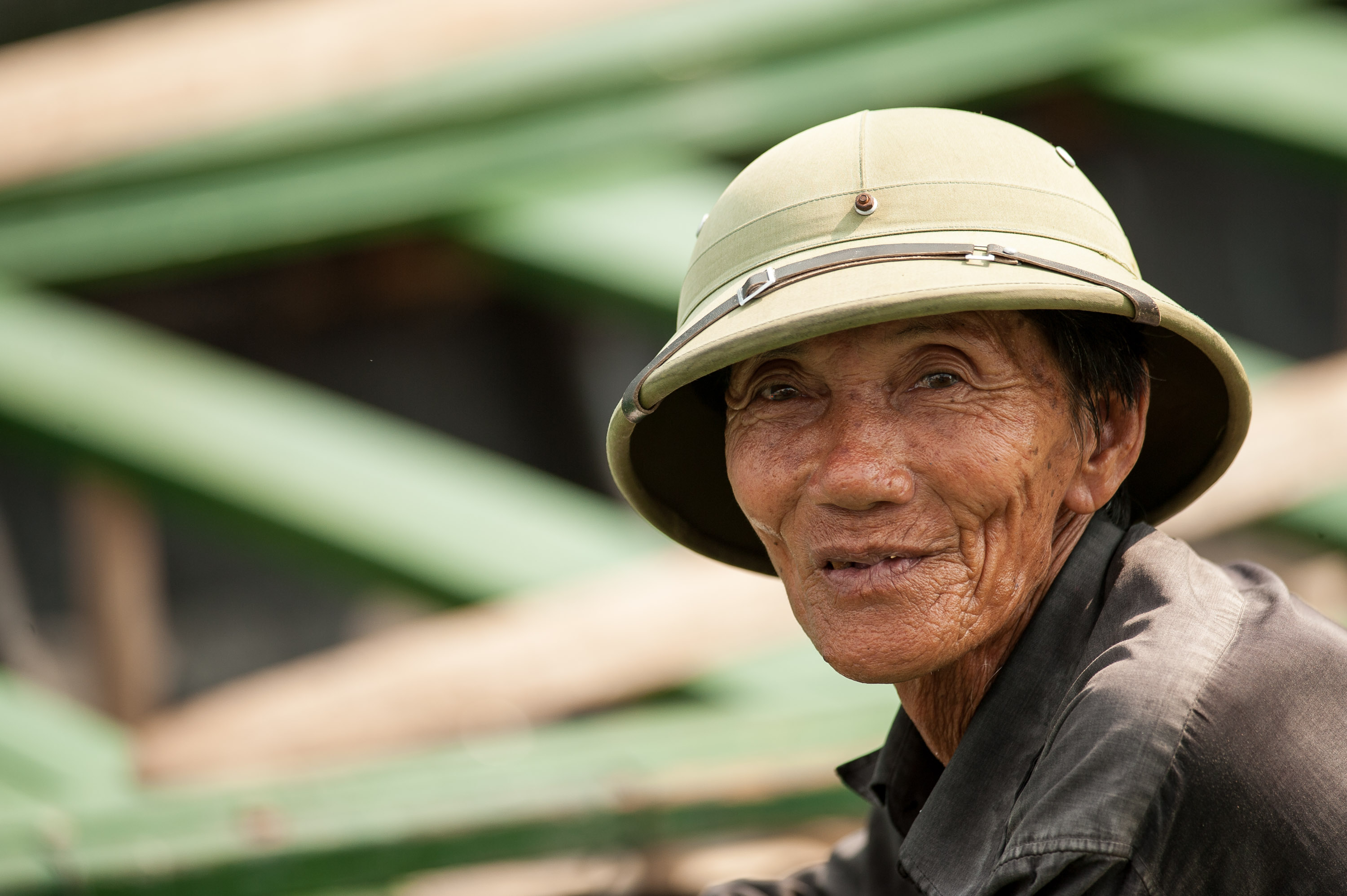 A man in a pith helmet smiles in Vietnam, with green scaffolding blurred behind him