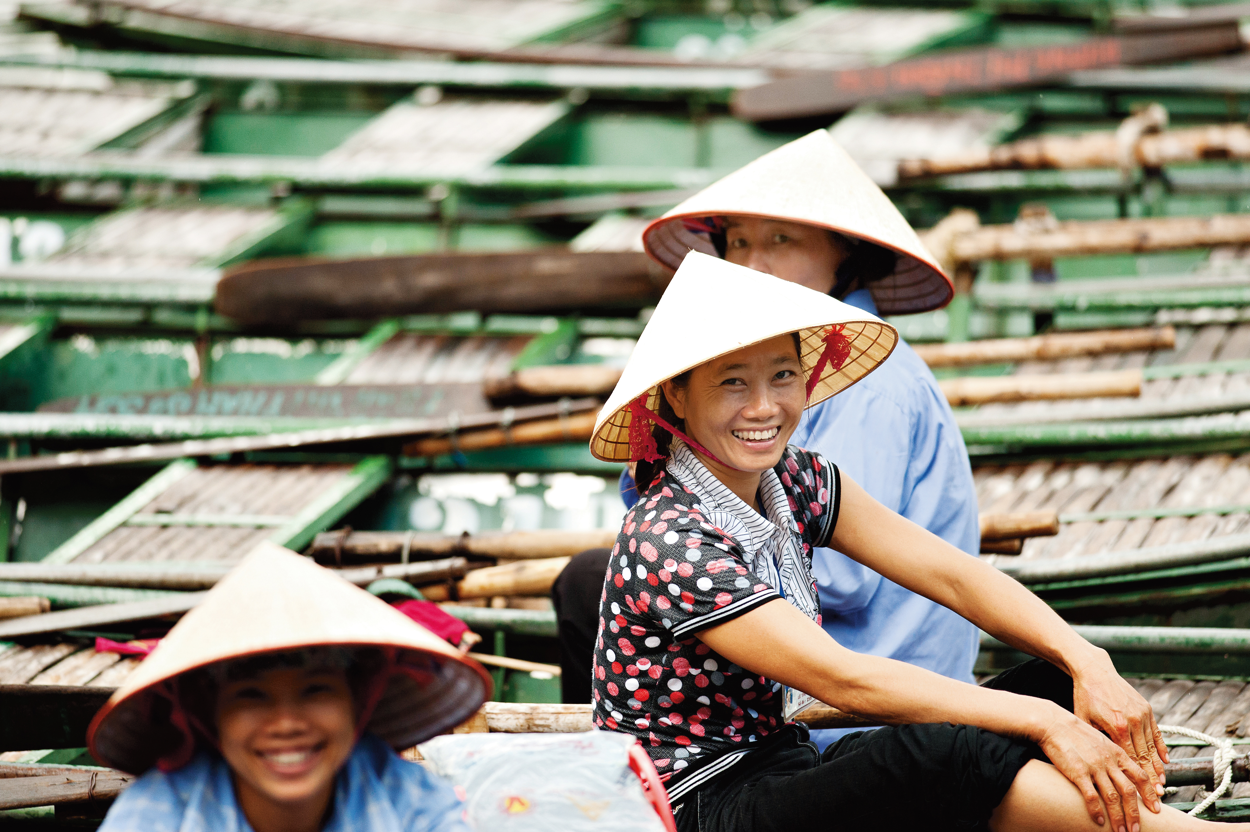 Women in conical hats sit among stacked wooden boats