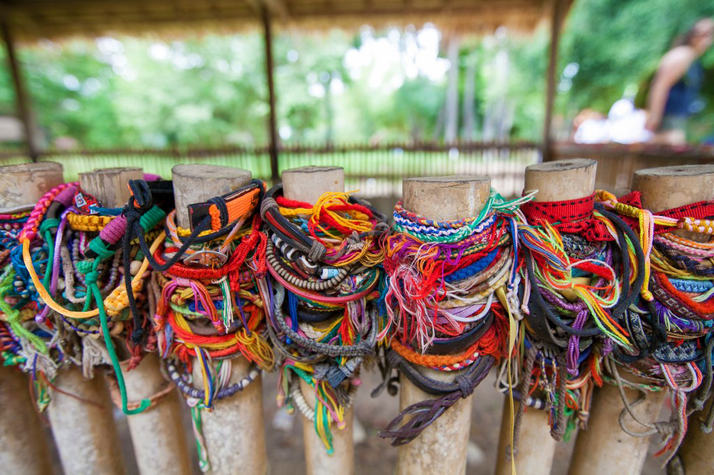 On a school trip, colorful woven friendship bracelets are tied to bamboo posts