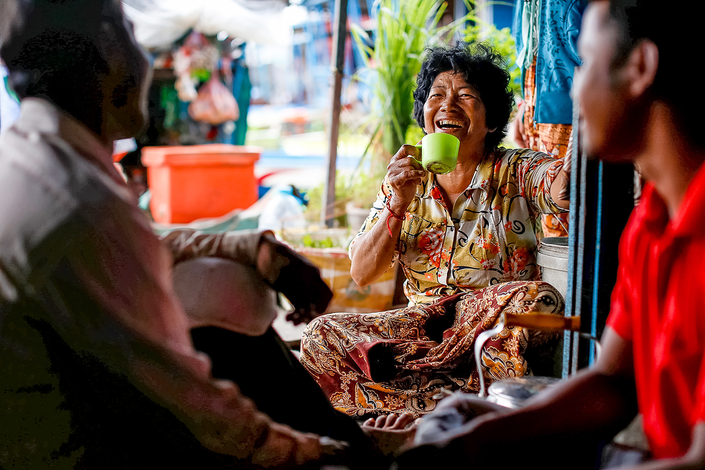 A woman laughs while sipping from a green mug during a conversation at home