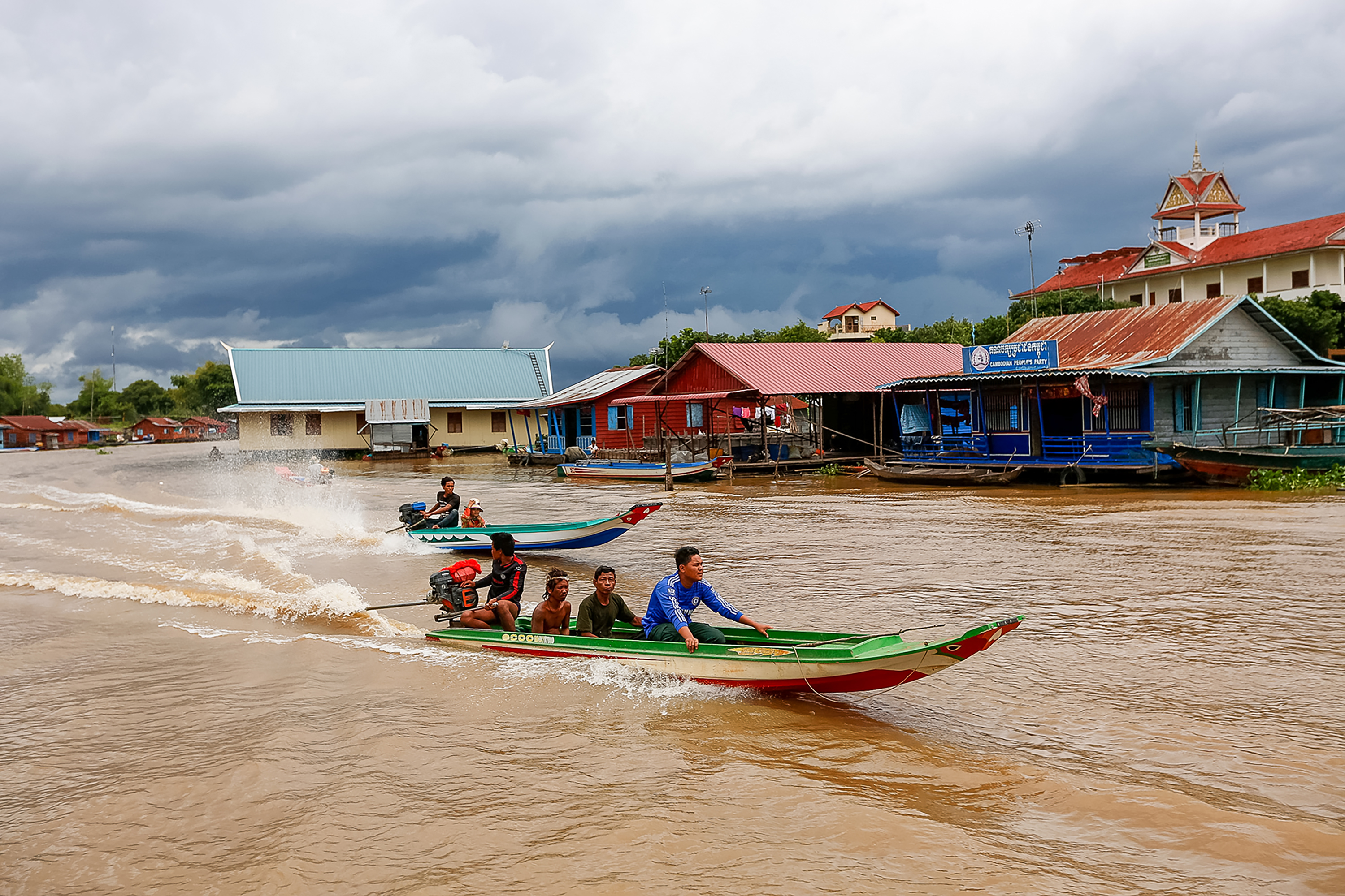 Long-tail boats speed across a river past floating houses in a village in Cambodia