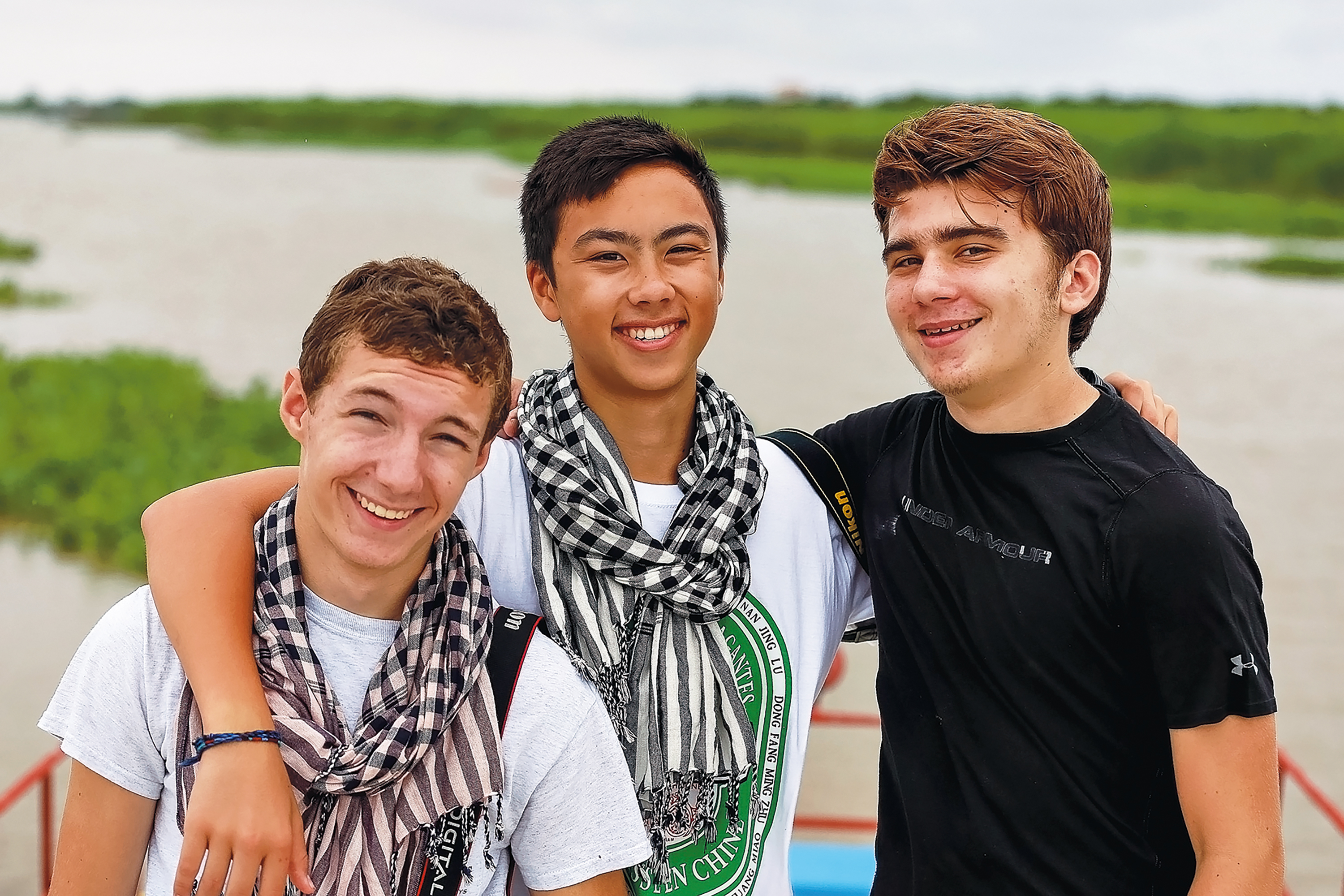 Students smile together on a boat with a flooded green landscape in Cambodia behind them