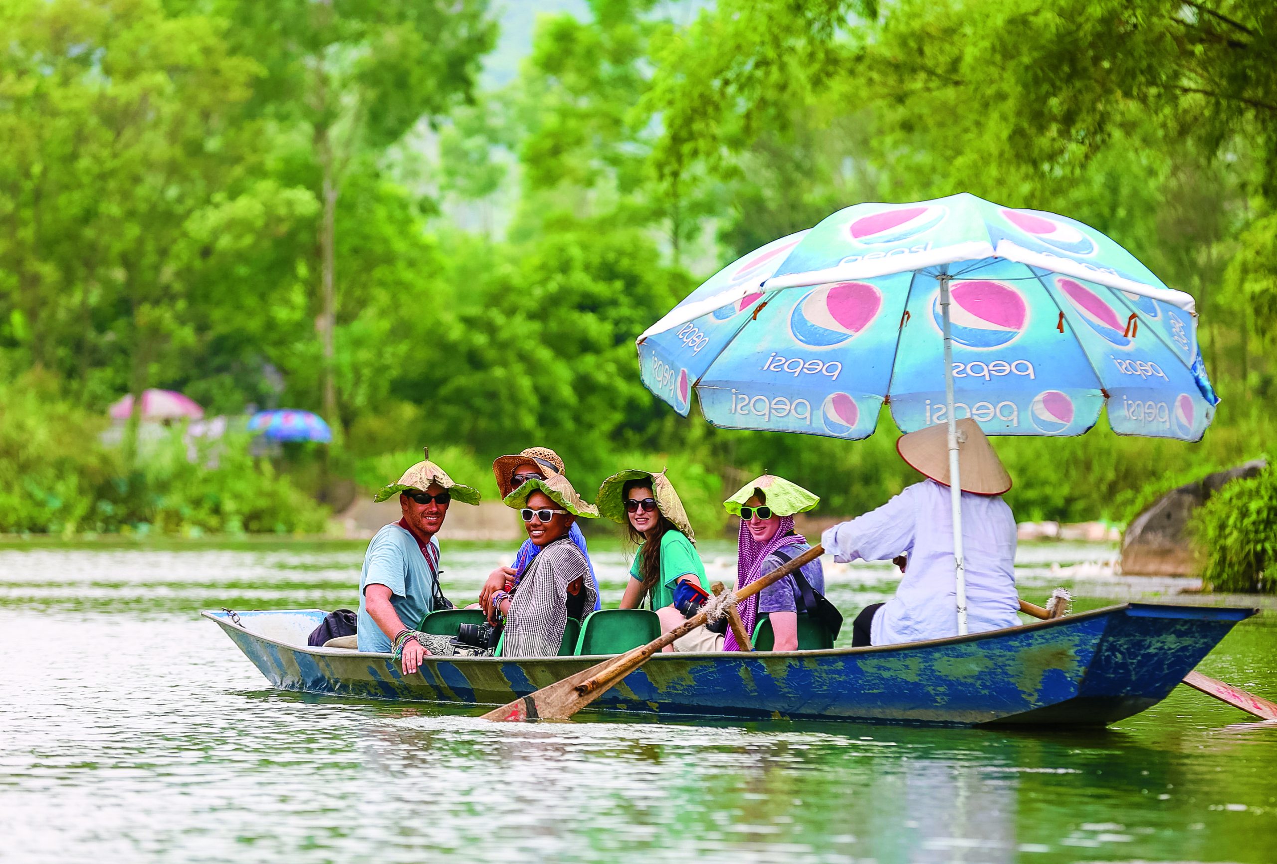 Group of tourists on a boat tour in Vietnam, shaded by a colorful umbrella.