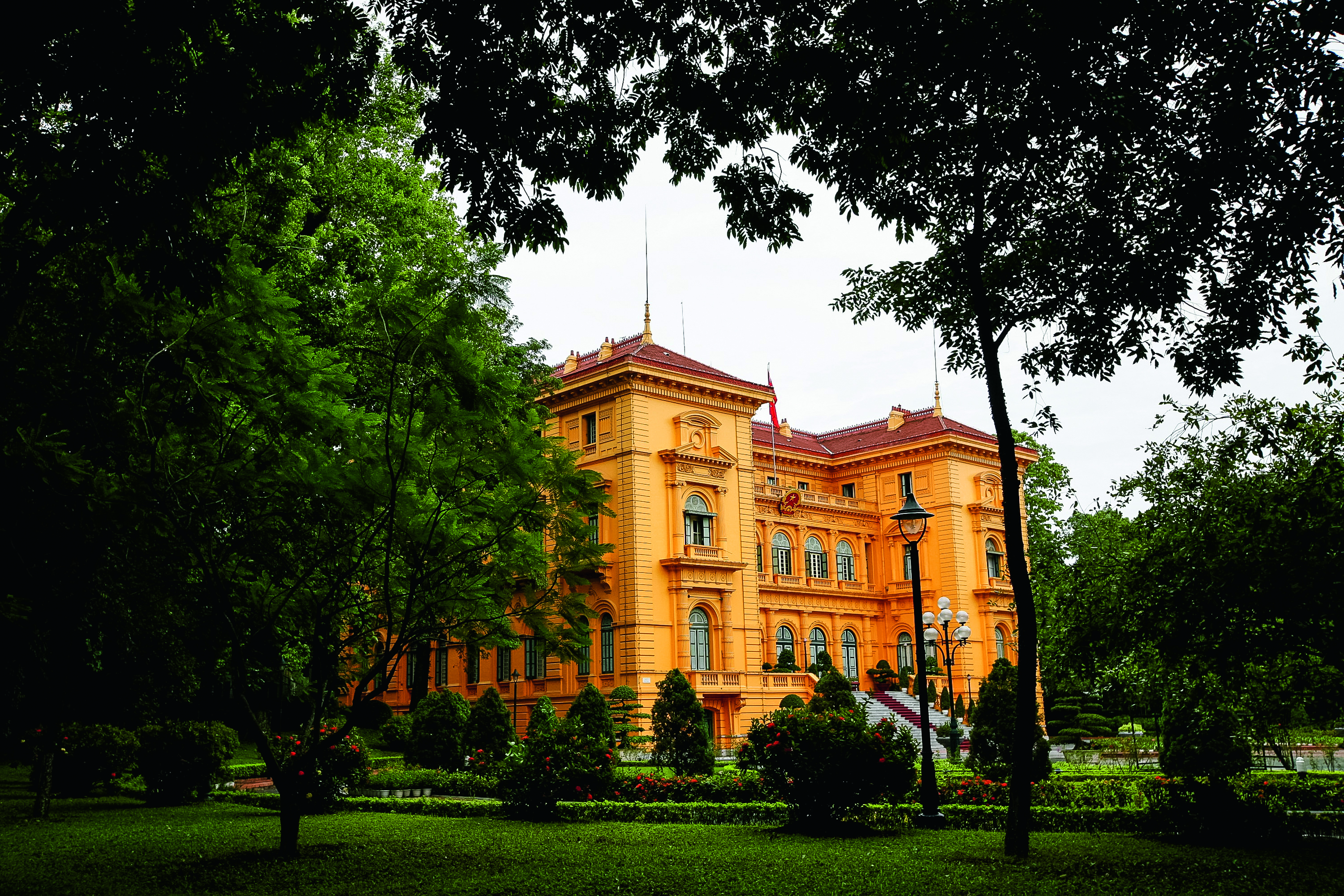 A yellow colonial-era palace surrounded by manicured gardens and trees in Hanoi