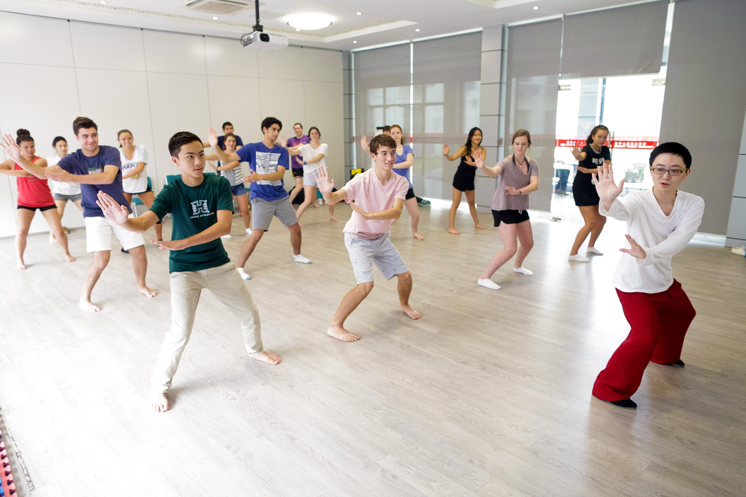 Students follow an instructor through a tai chi stance in a bright studio