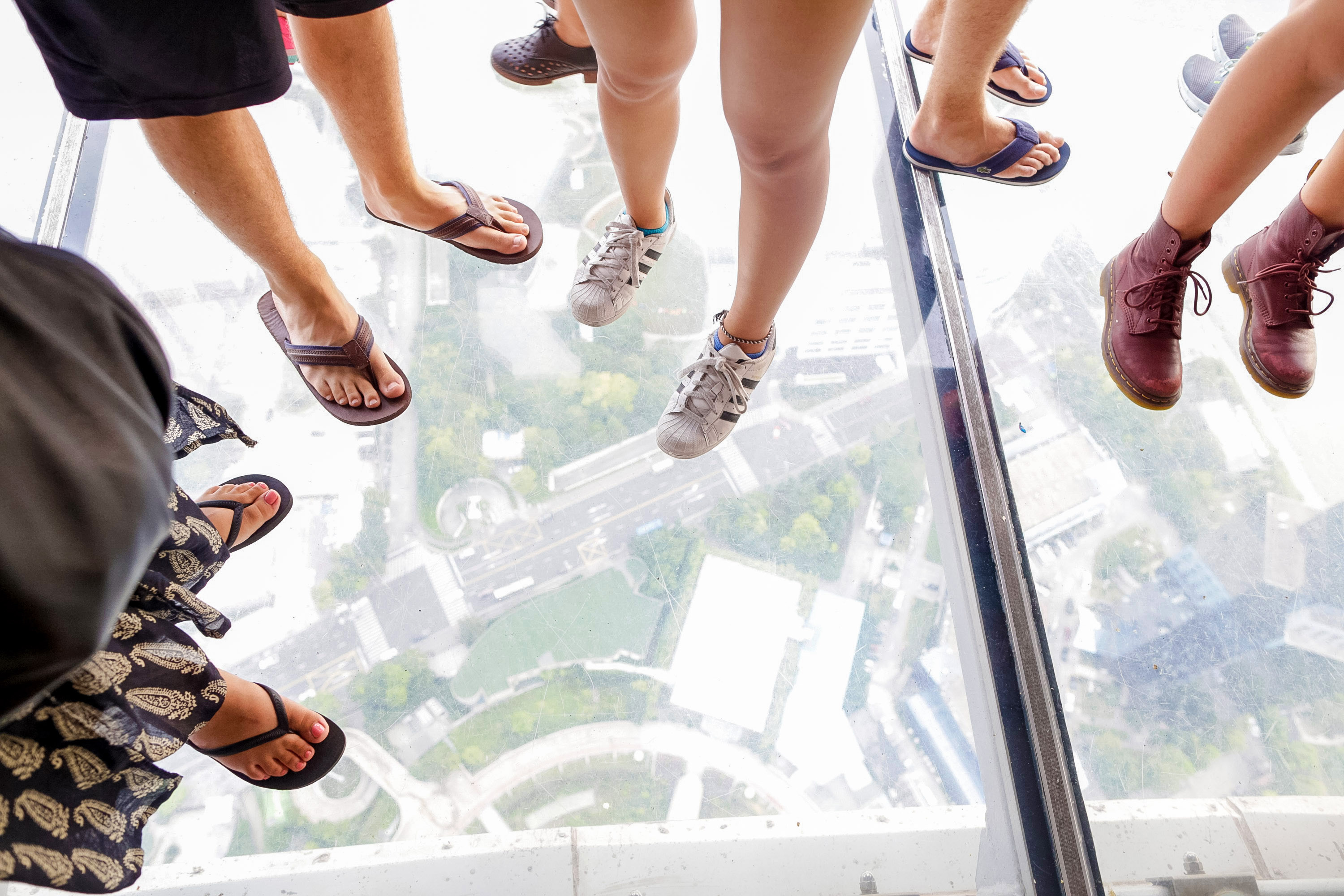 Feet stand on a glass observation floor high above a city