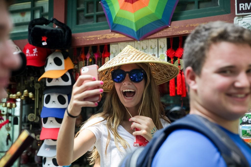 A student taking a photo in a colorful shopping street during a summer program for high school students in China with Rustic Pathways.