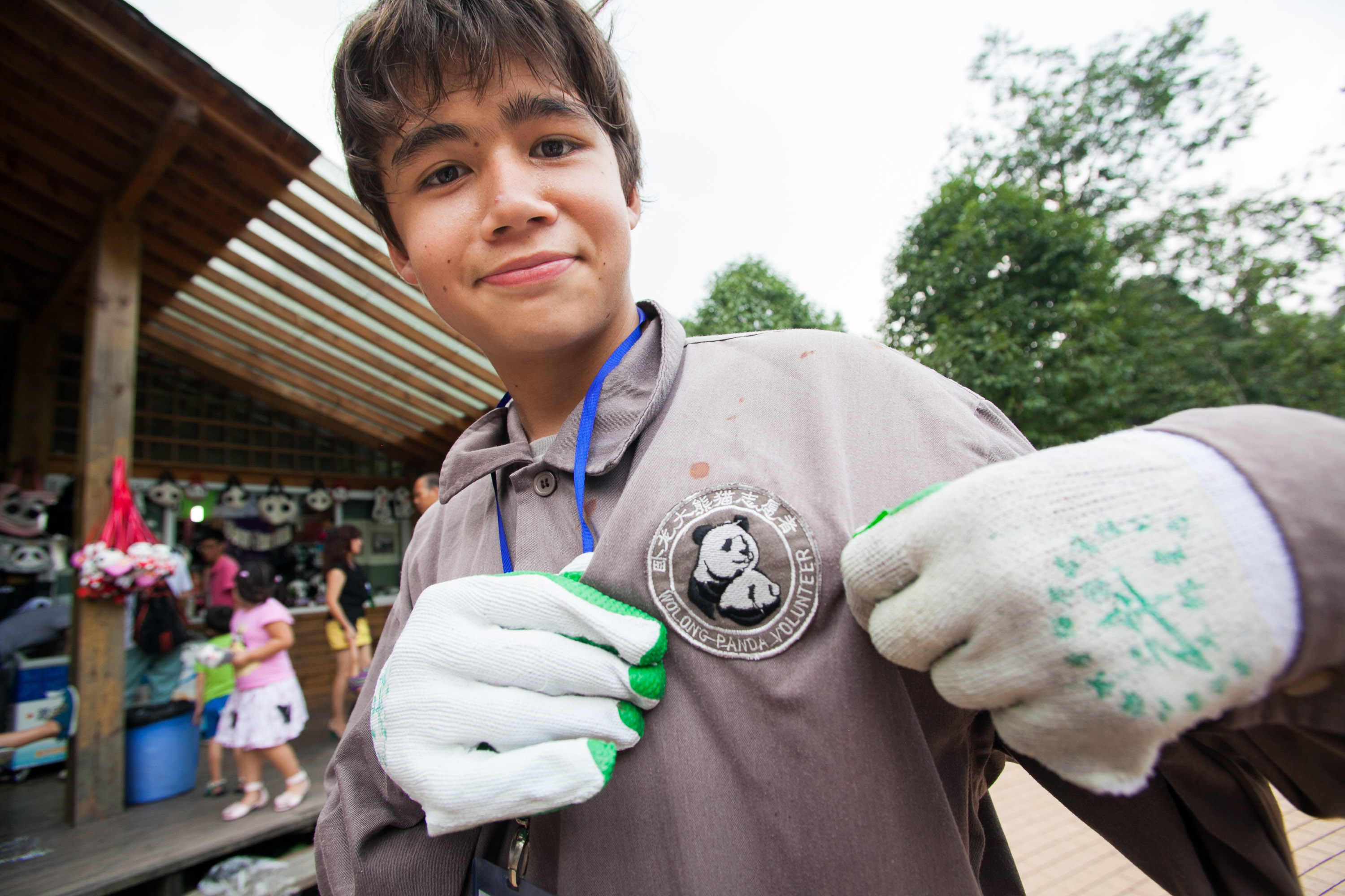A student wearing a panda badge and work gloves gestures toward the camera at a conservation center