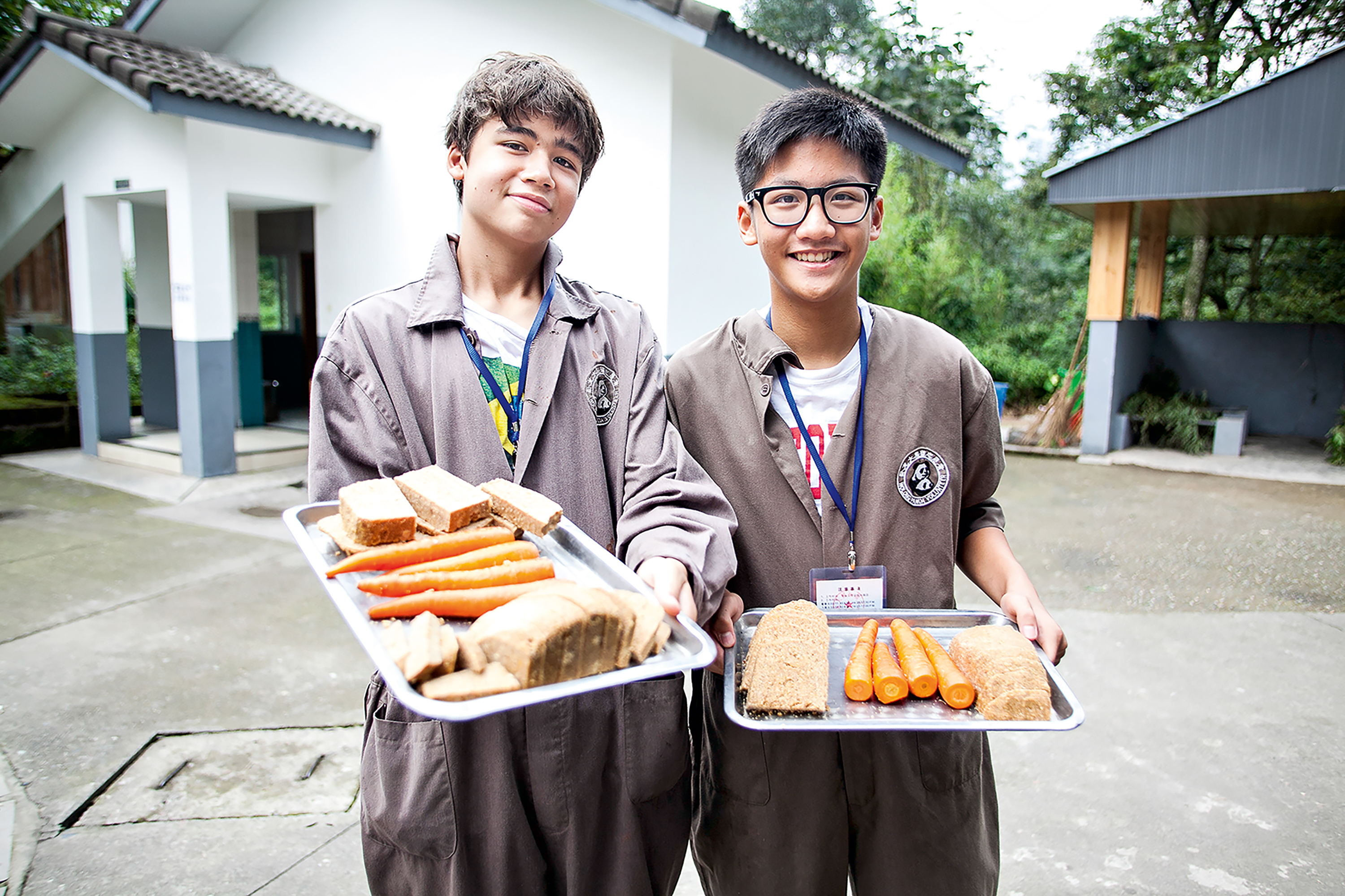 Students in coveralls hold trays of panda food outside a building in China