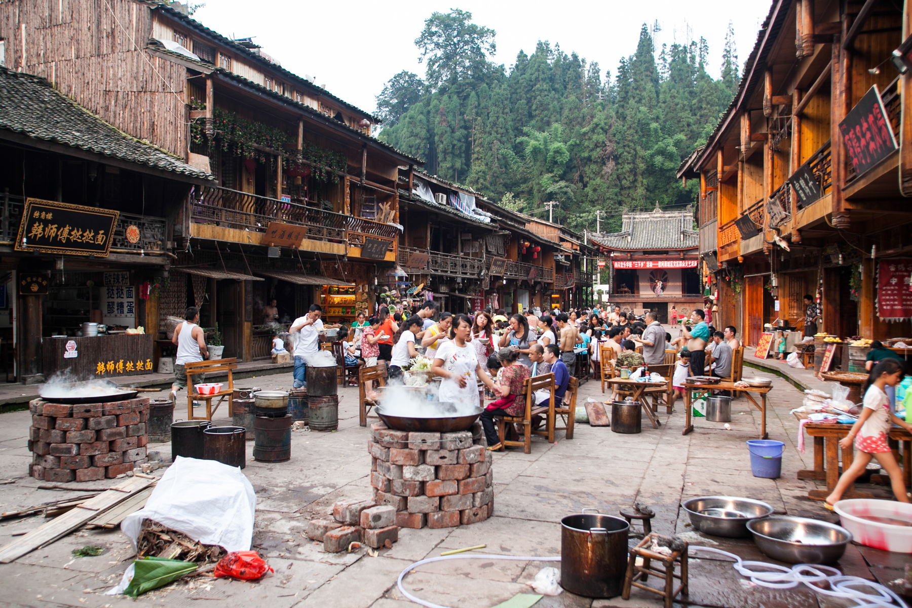 Outdoor cooking pots and market stalls fill a busy street in a traditional Chinese town