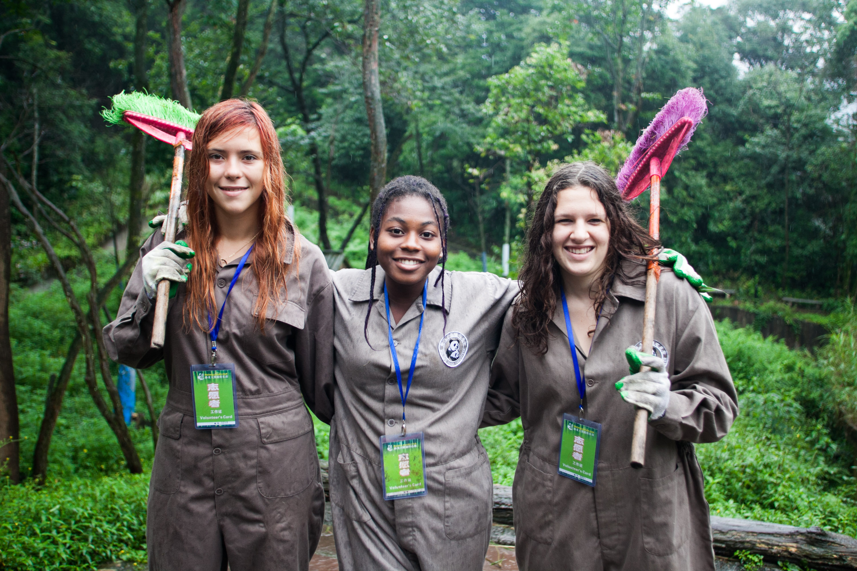 Students in coveralls smile while holding cleaning brushes in a forested area