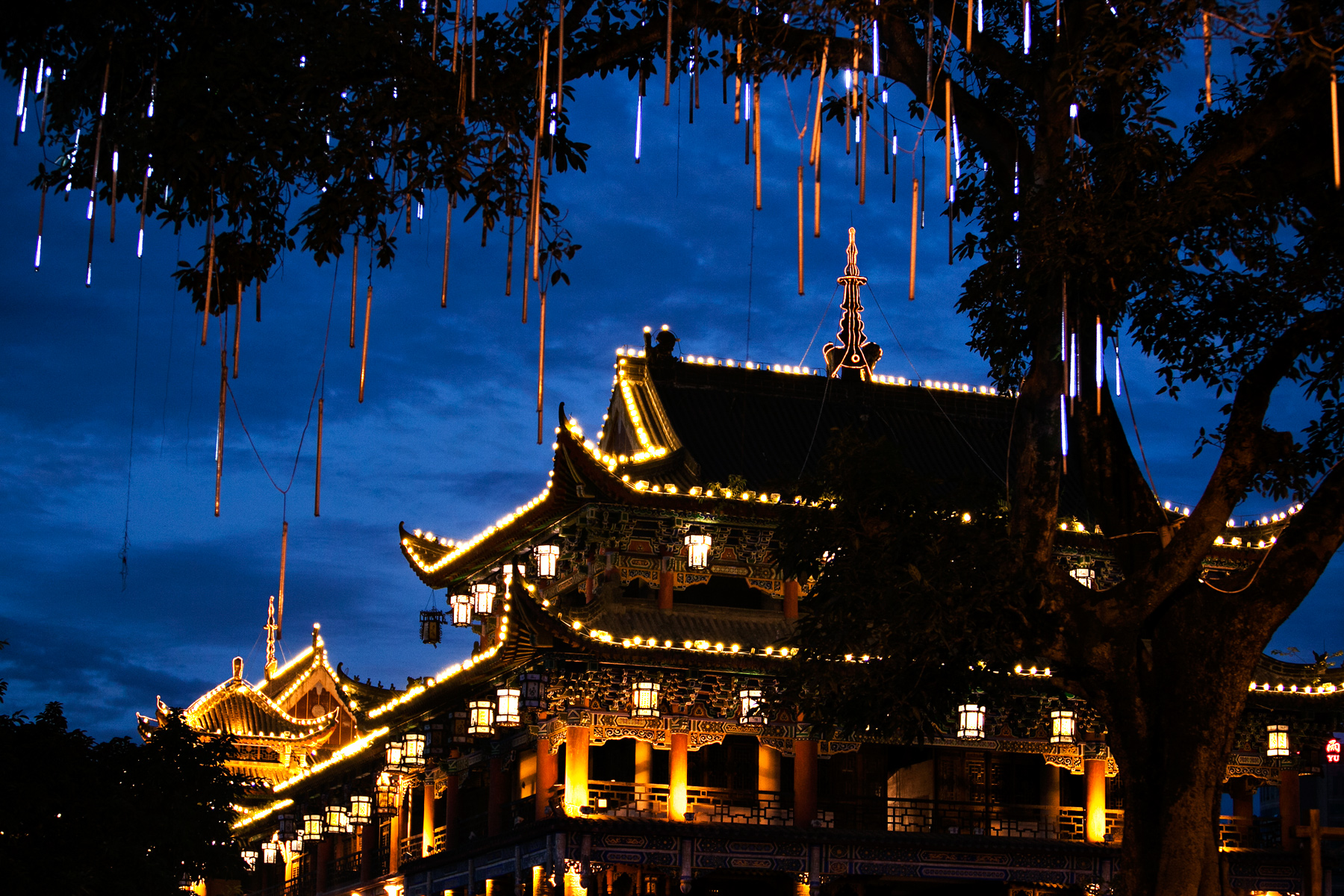 A traditional Chinese temple glows at night beneath string lights hanging from tree branches