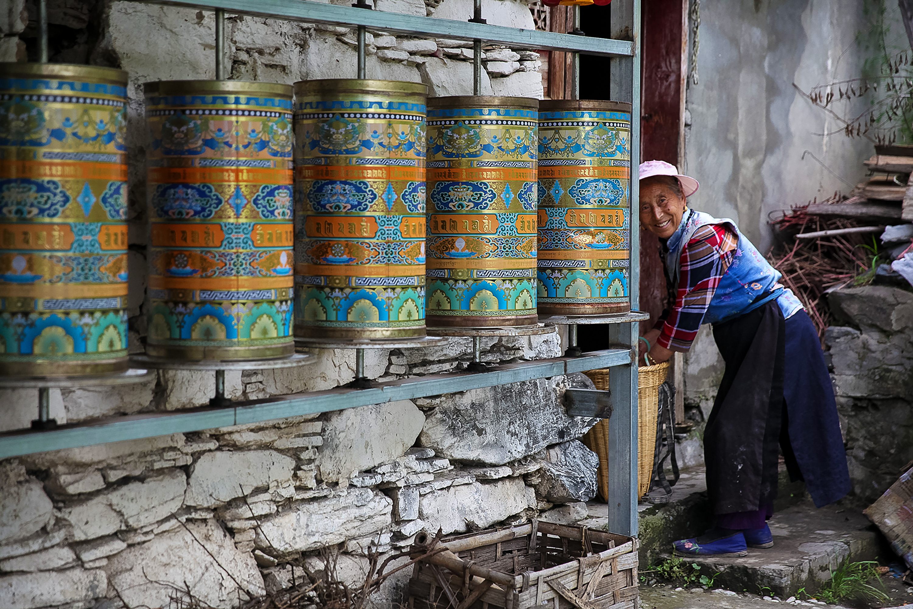 Colorful prayer wheels line a wall as a local woman smiles nearby