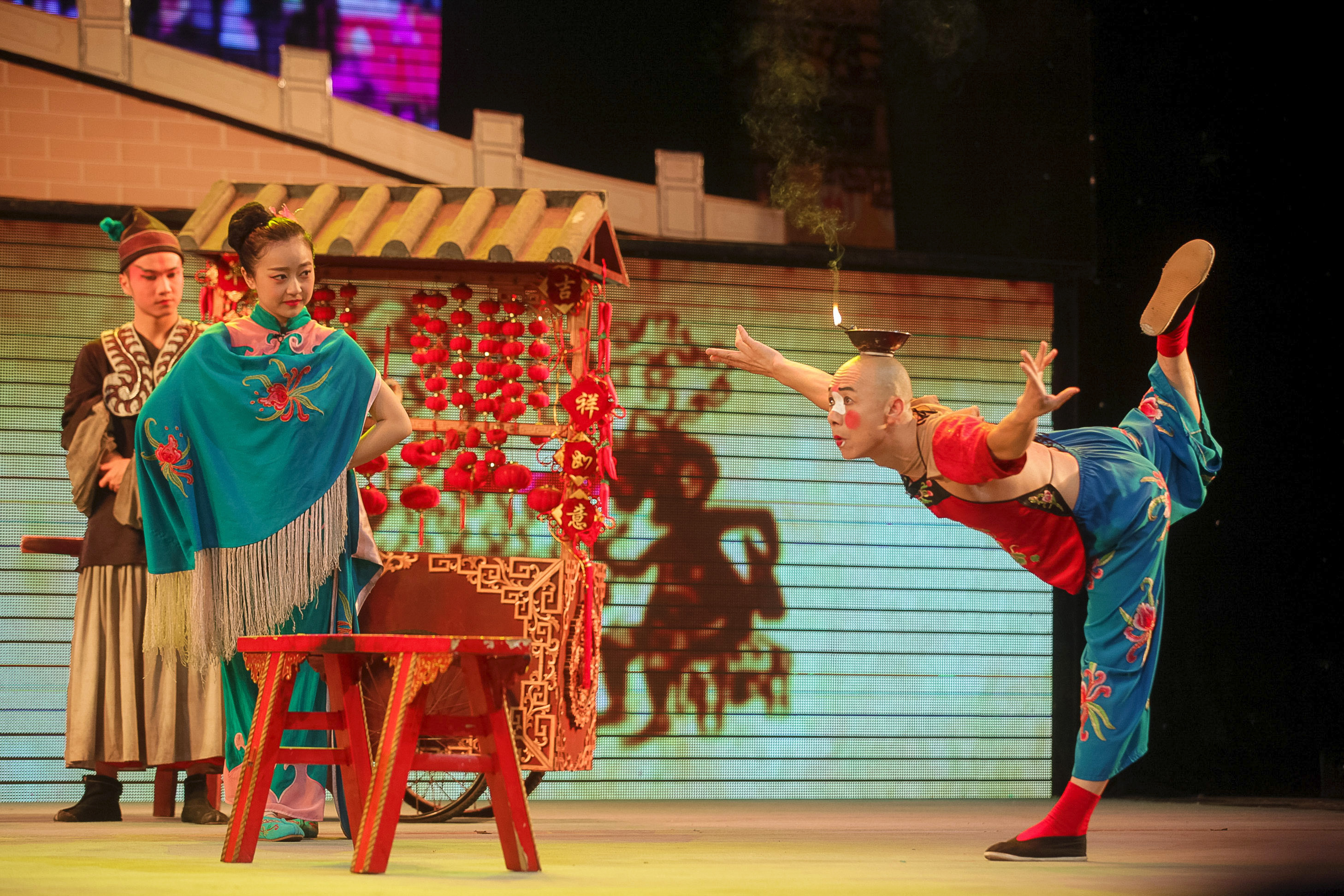 A performer balances in a stage acrobatics act while others in costume look on