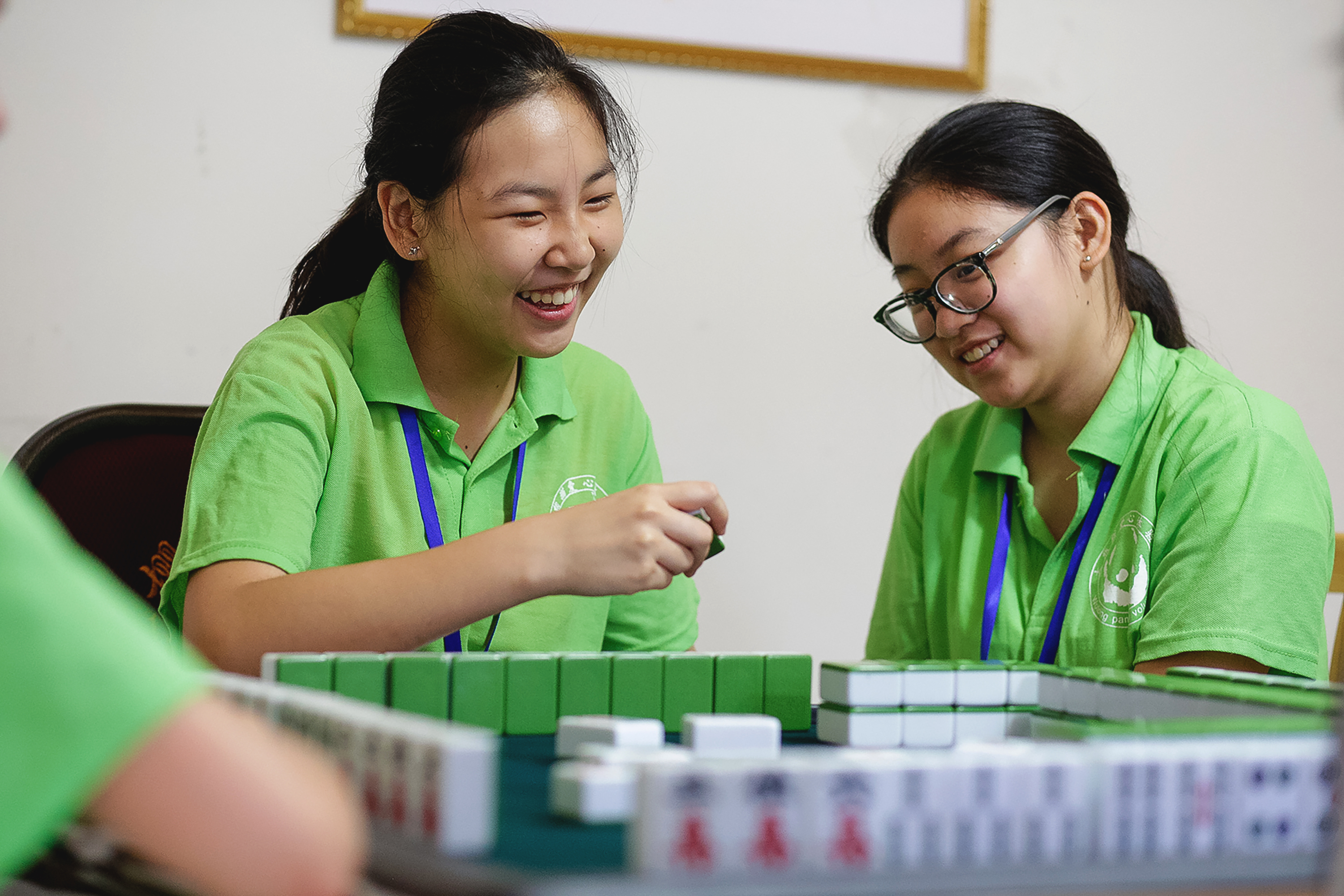 Students in green polos laugh while playing mahjong