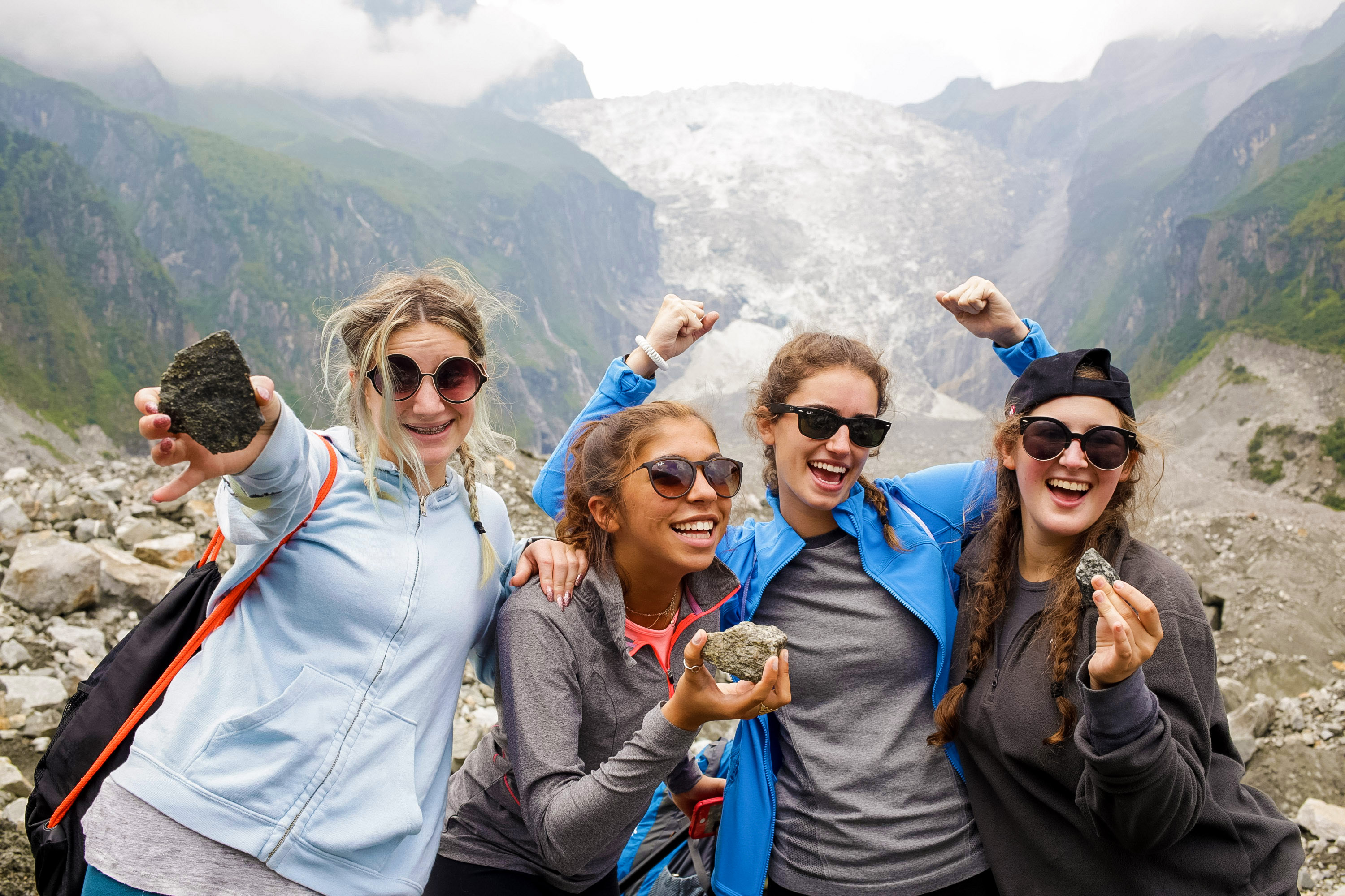 Students cheer and hold rocks in front of a glacier valley