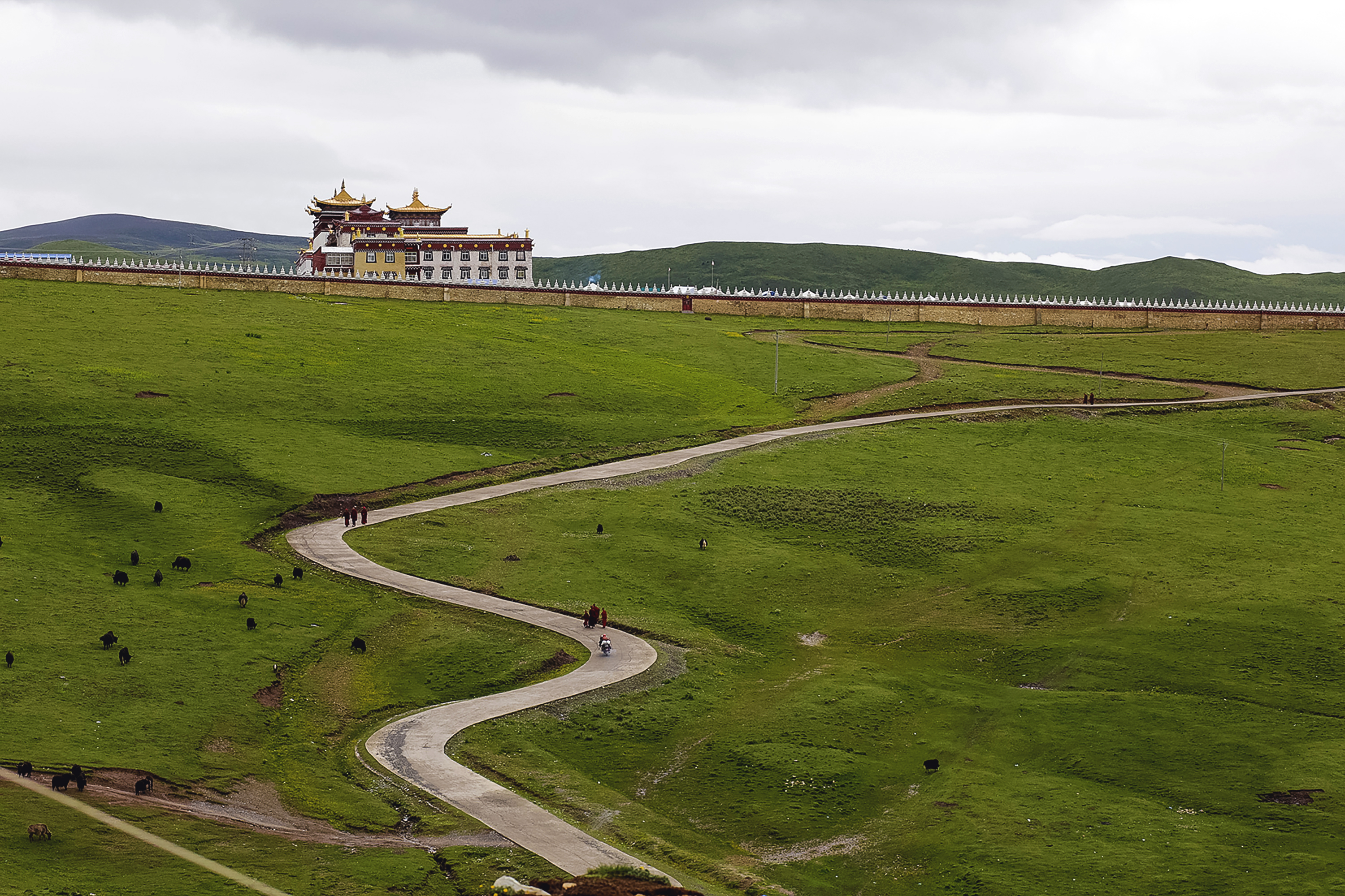 A winding path crosses green grassland leading to a monastery building in the distance