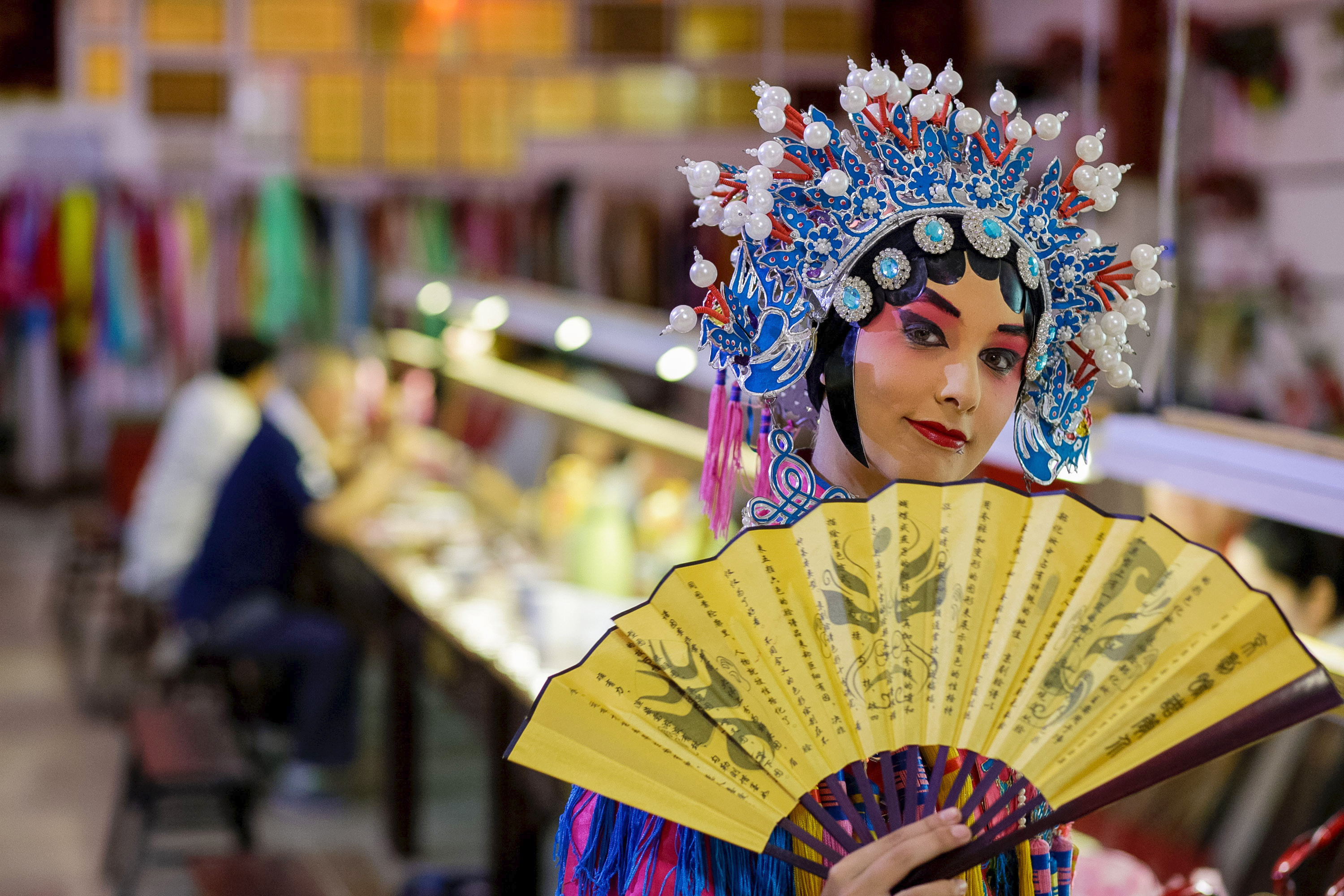 A performer in traditional Chinese opera makeup and headdress holds a painted fan
