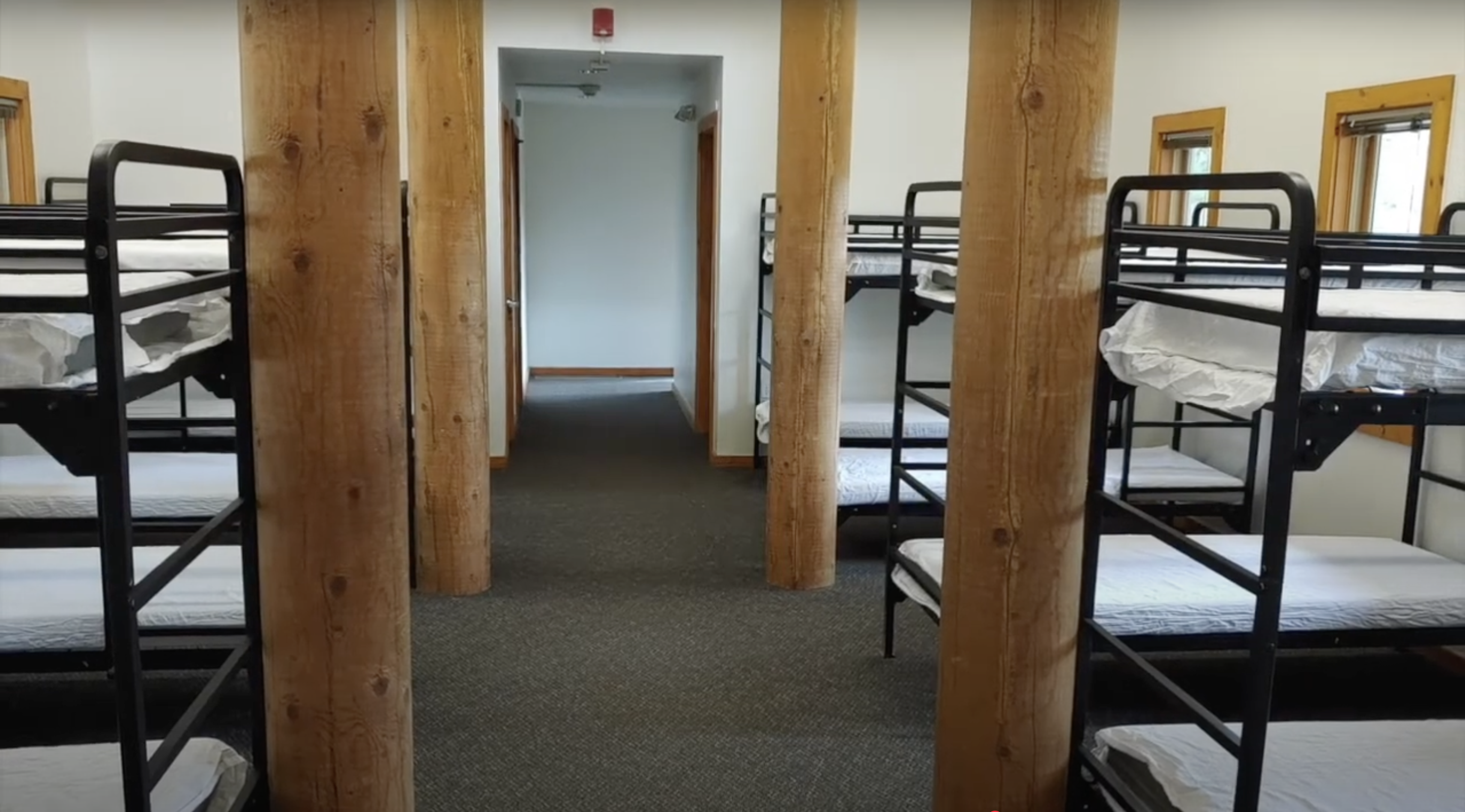 Empty bunk beds line a cabin hallway supported by wooden posts