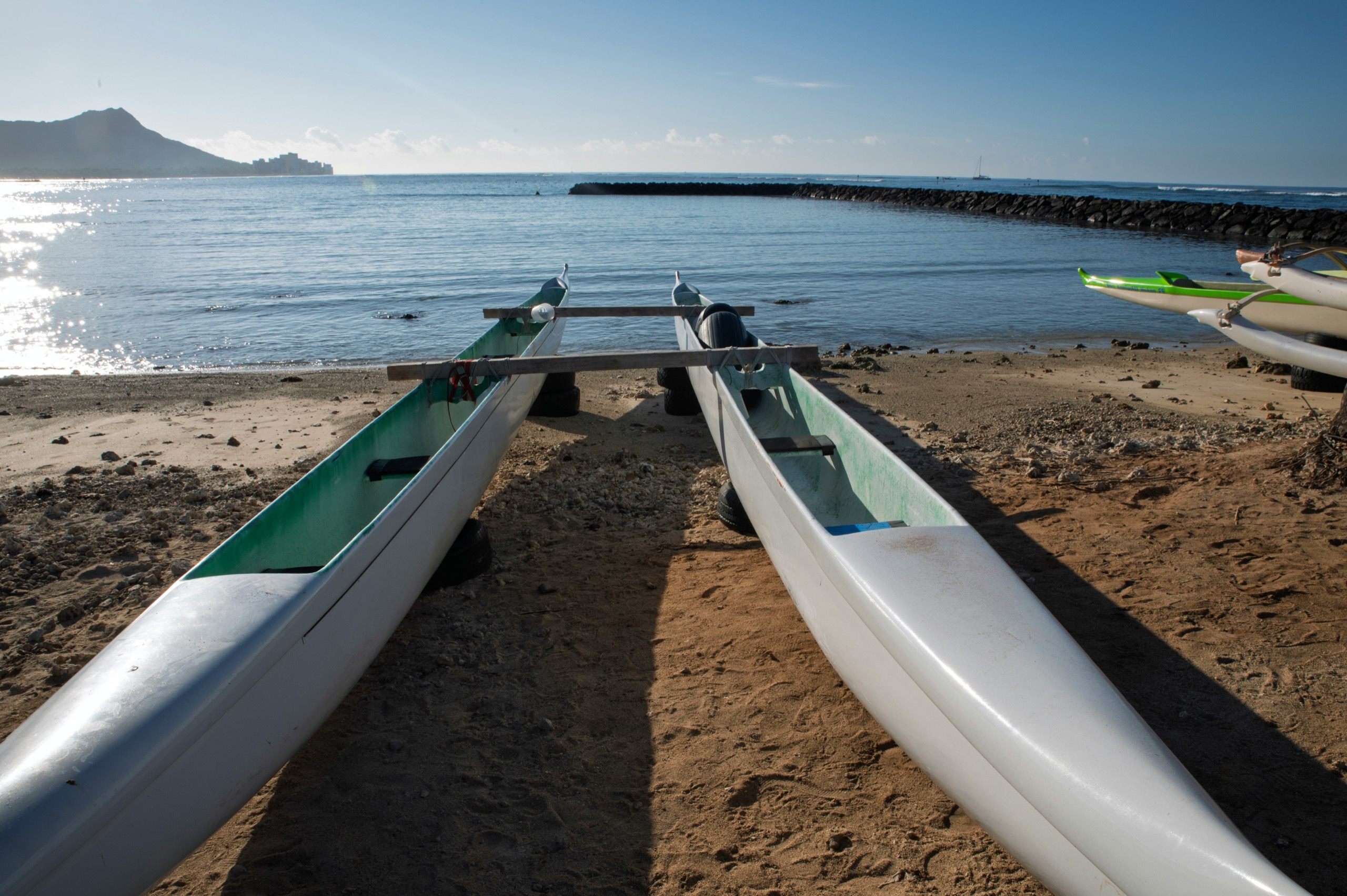Two outrigger canoes rest on a beach with calm ocean and a distant headland.