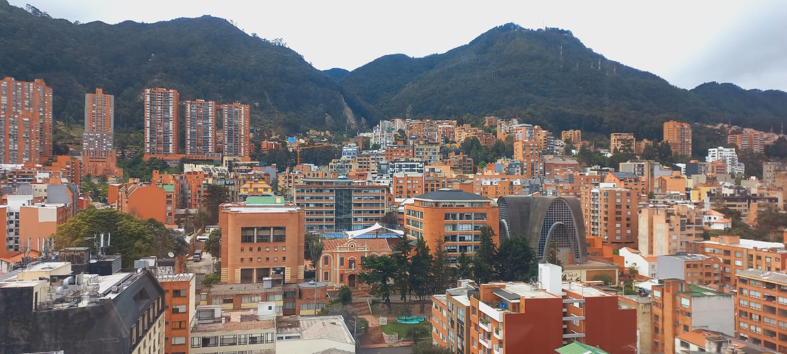 Terracotta apartment towers of Bogotá's Chapinero district climb a green hillside beneath the mountains.